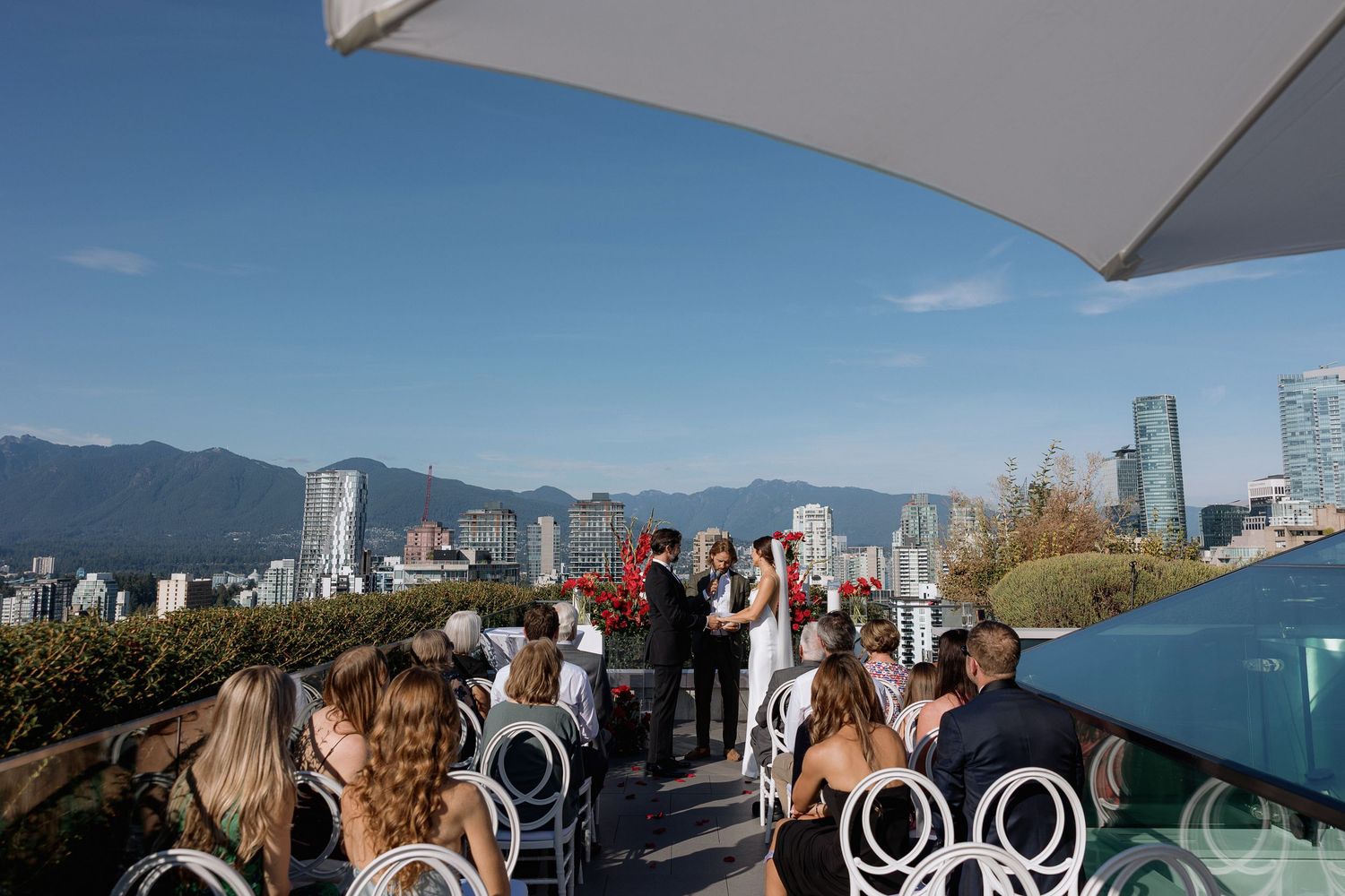 Group of people enjoying scenic views of Vancouver's skyline and mountains from a rooftop patio on a sunny day.