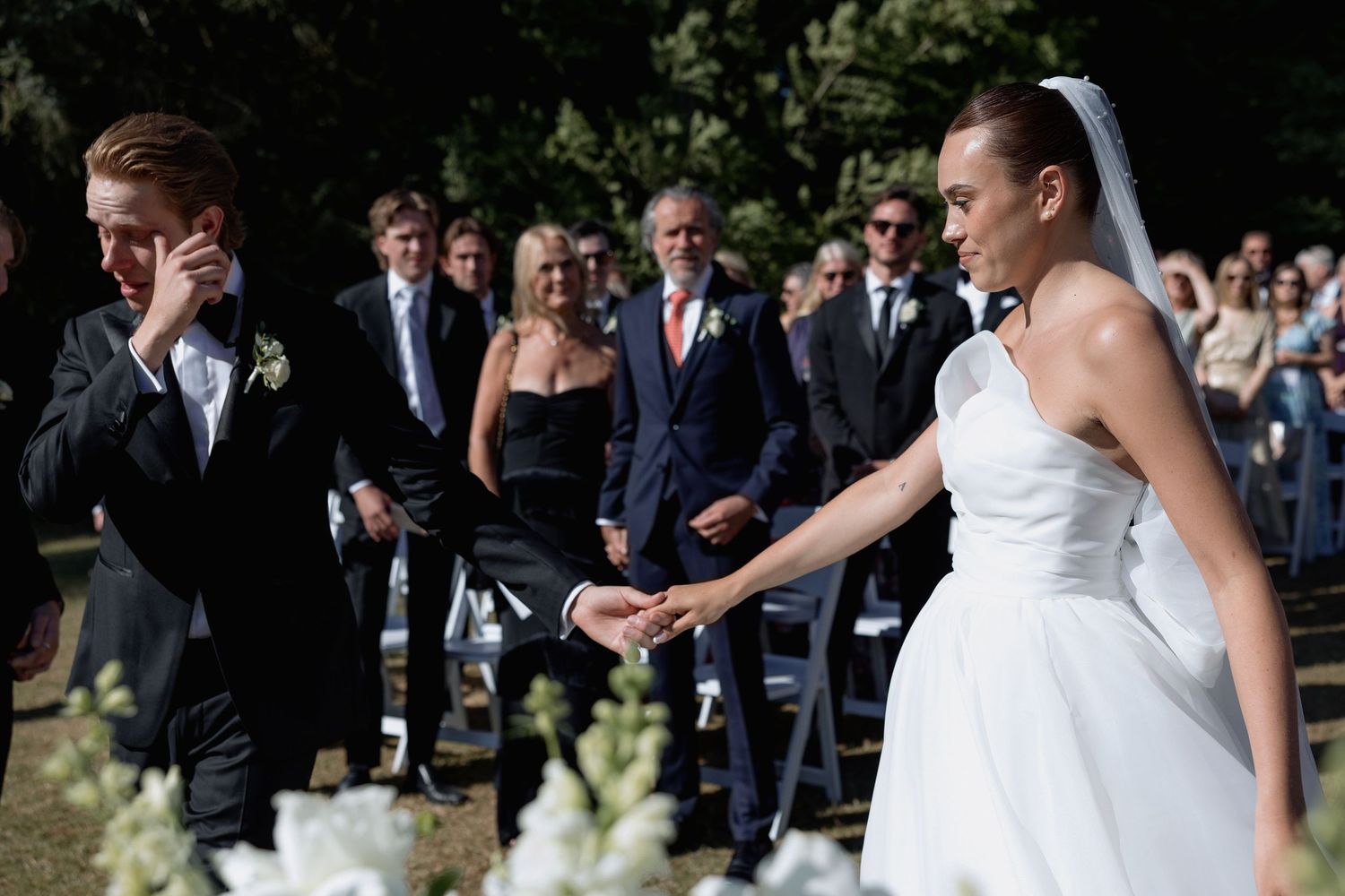 Wedding ceremony guests seated in white chairs on a lawn.
