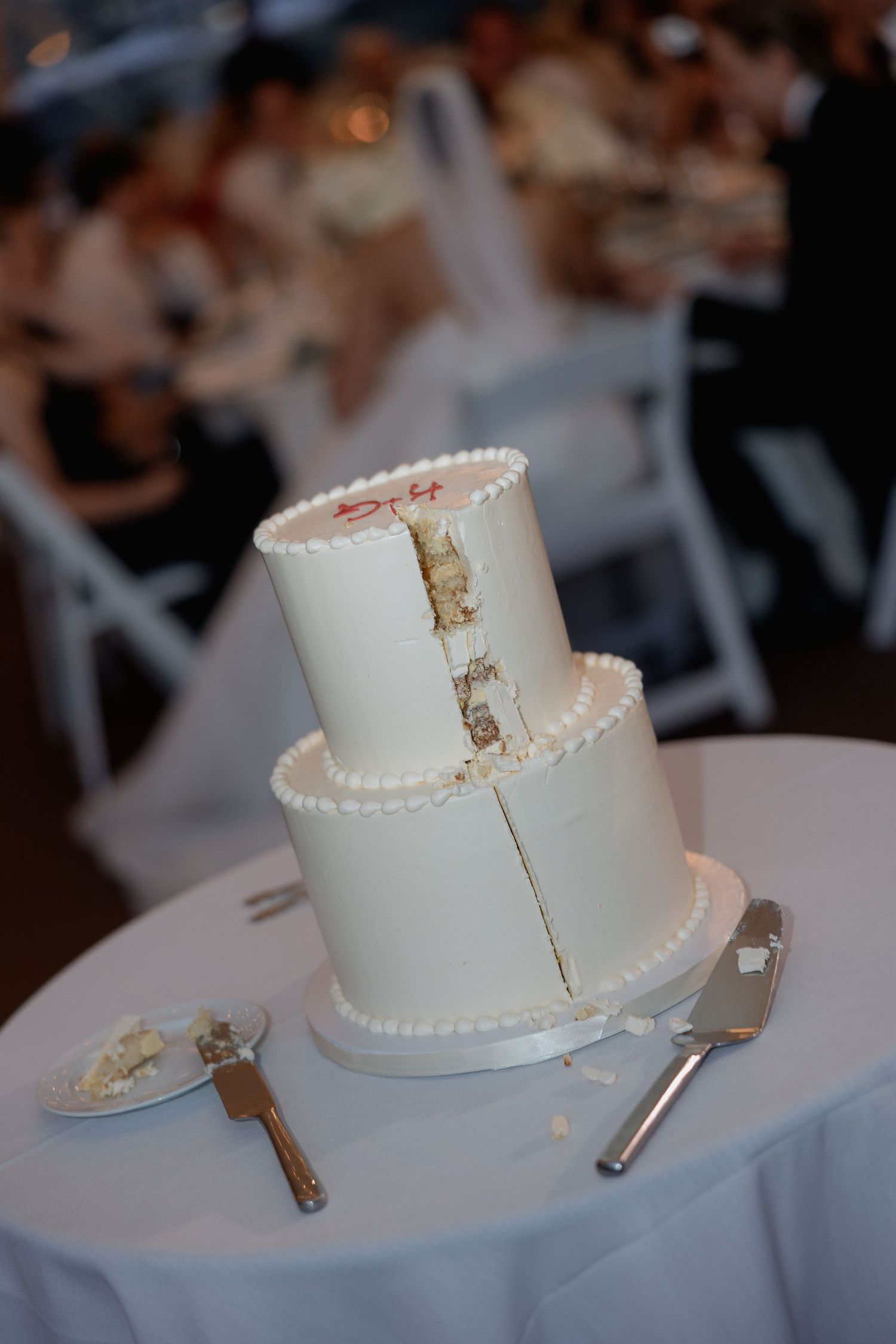 White tiered wedding cake falling over on a table covered with white linens.