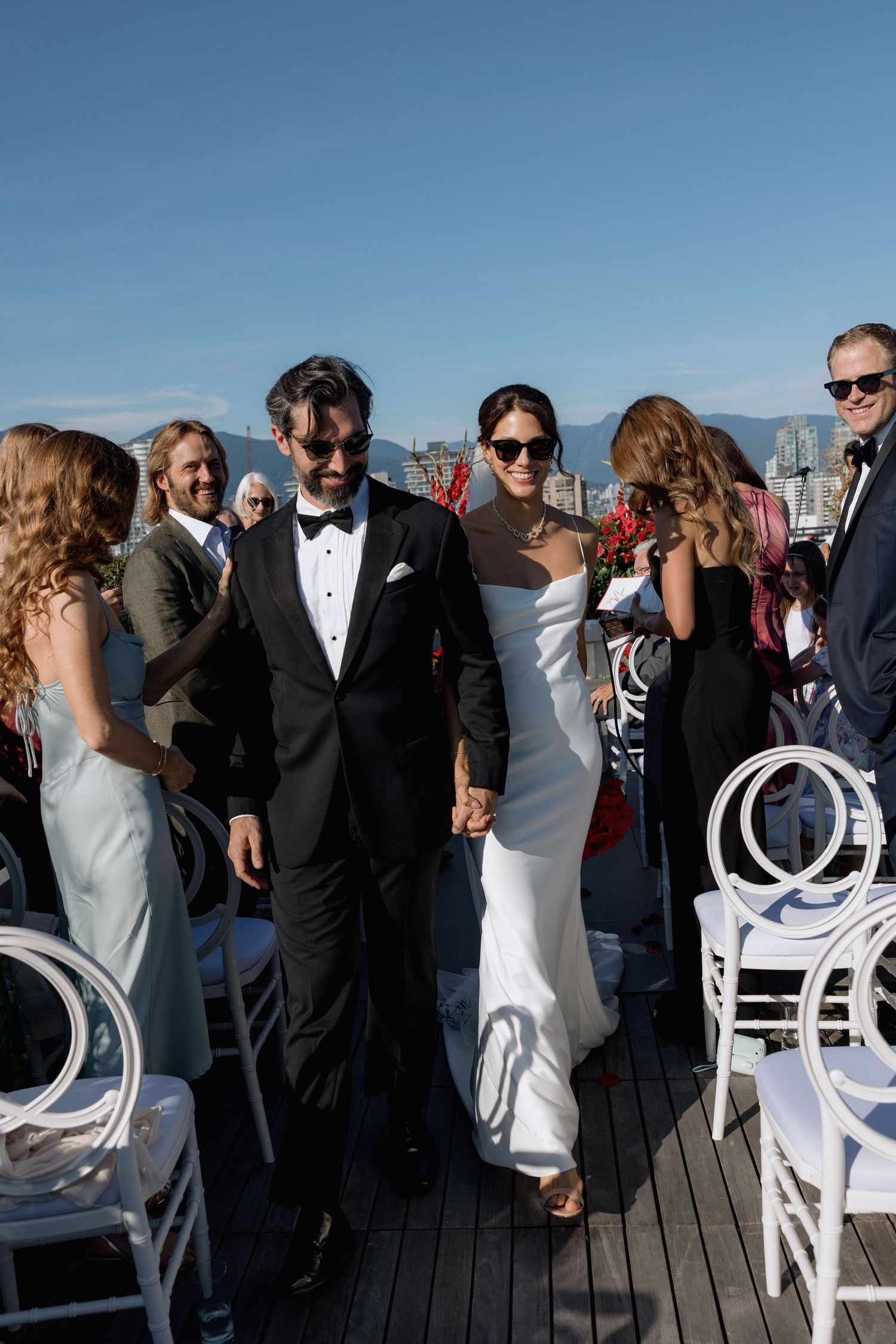 Wedding guests mingling on a rooftop deck with white chairs and mountain backdrop.