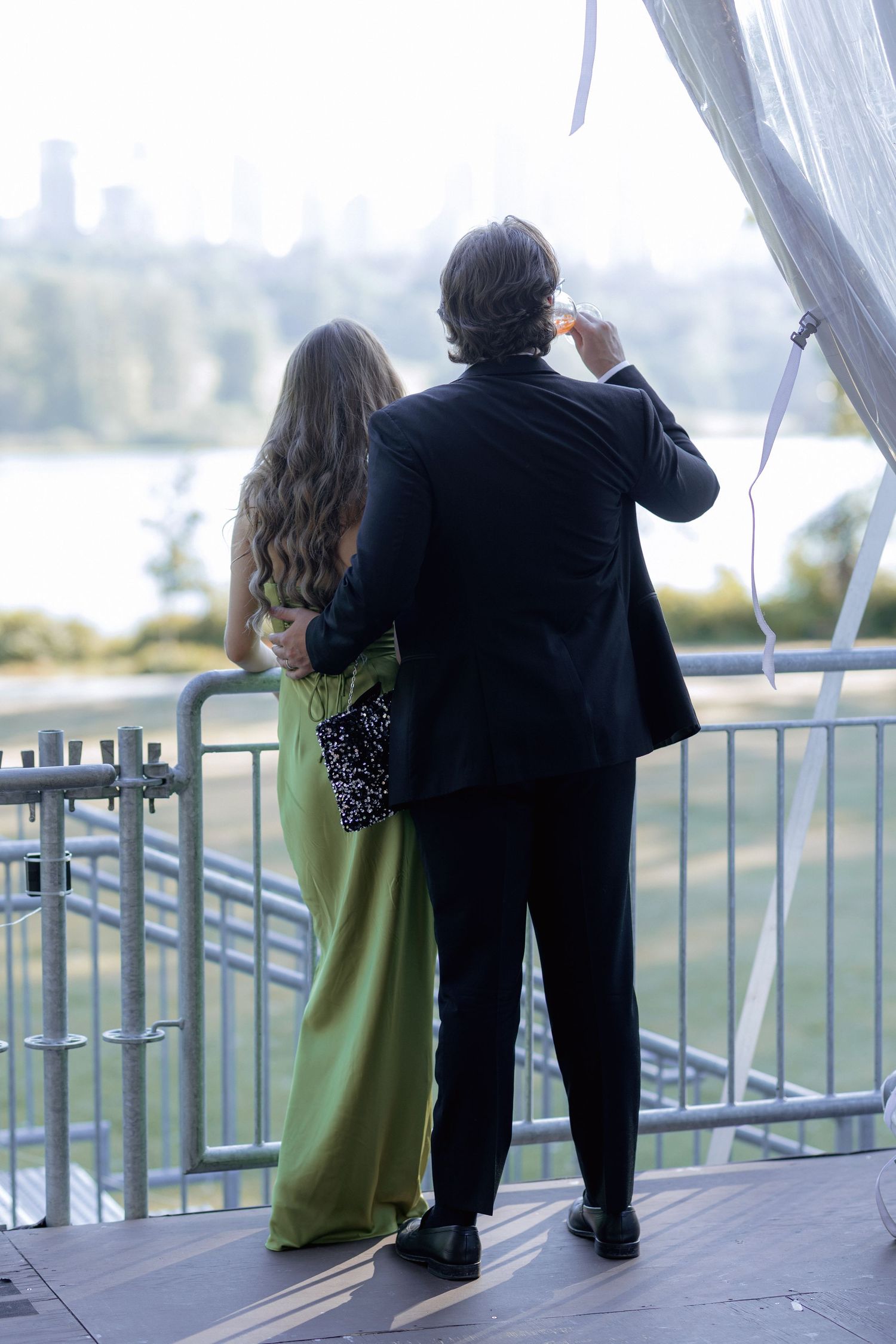 Couple in formal attire admiring the view from a balcony overlooking water.
