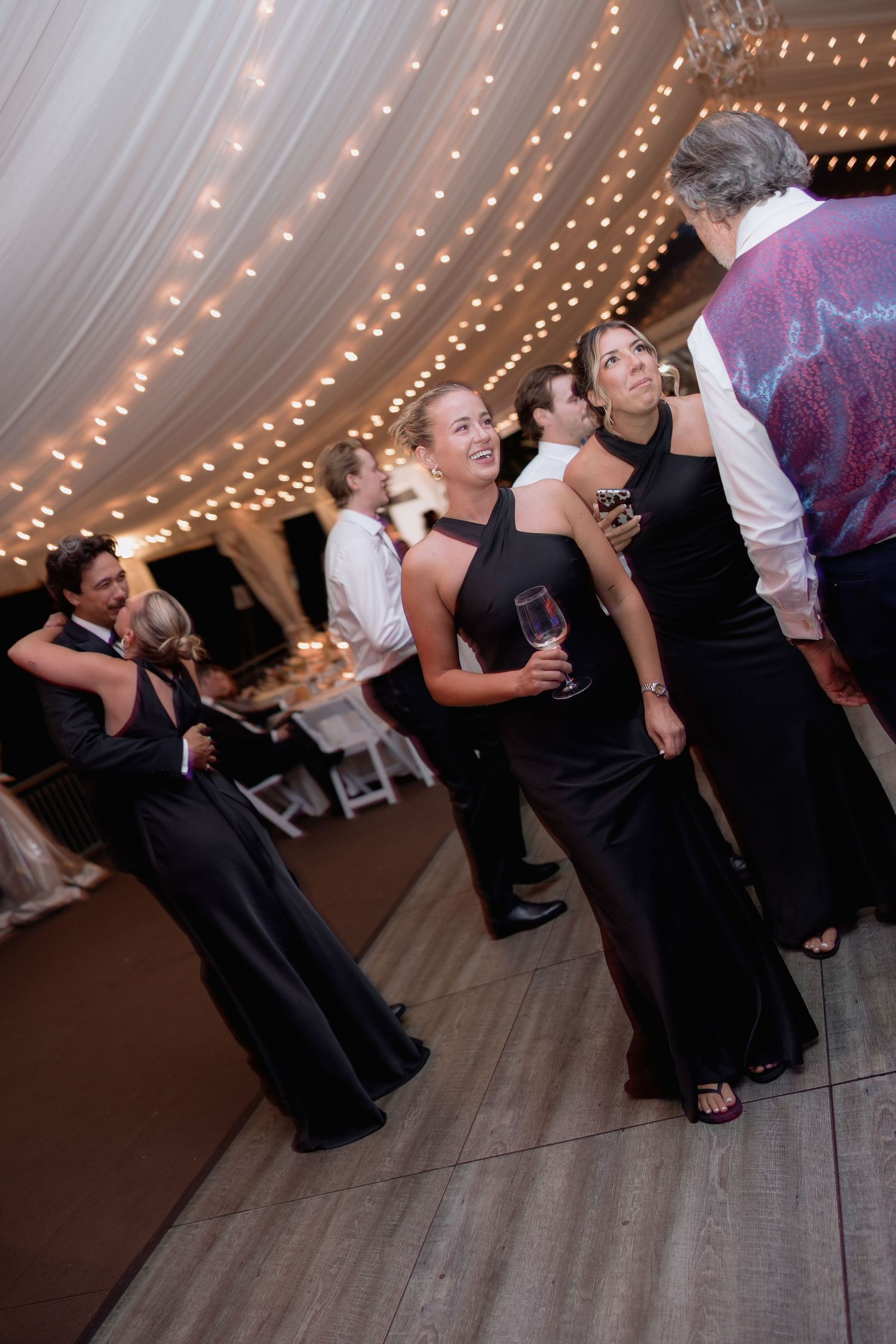 Guests showing off dance moves on a wooden floor under elegant tent lighting.