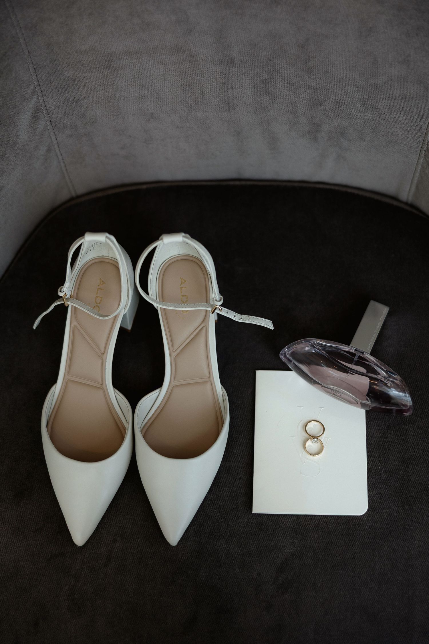 White bridal shoes and wedding rings arranged on dark background.