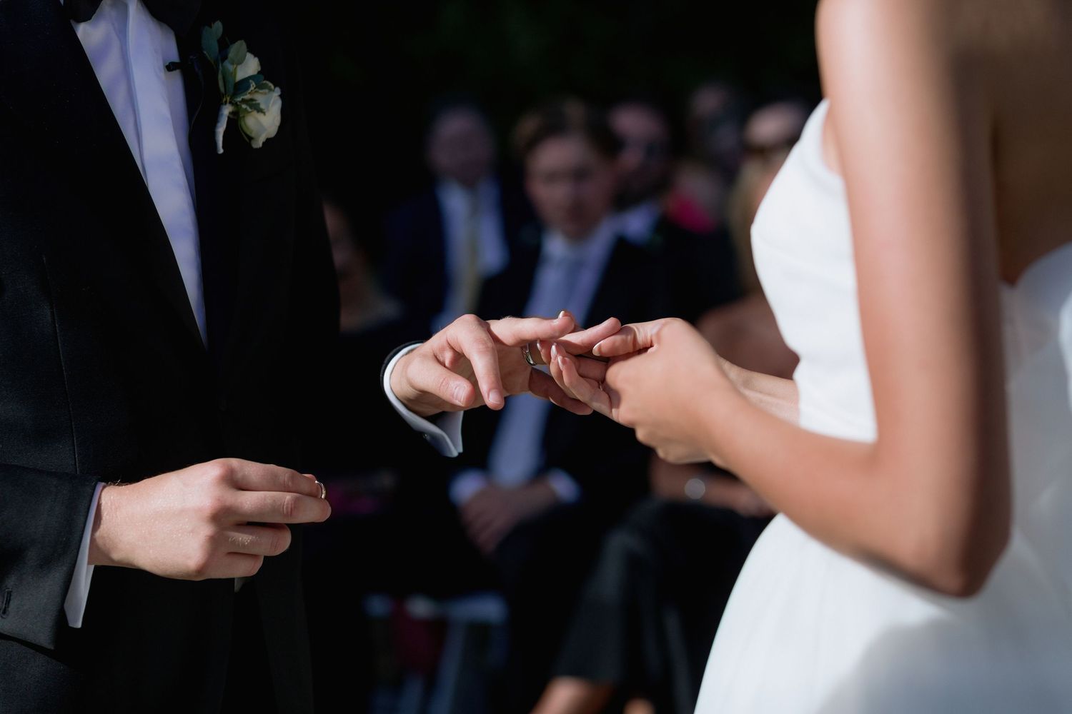 Wedding ceremony guests seated in white chairs on a grassy lawn with a city skyline visible in the background.