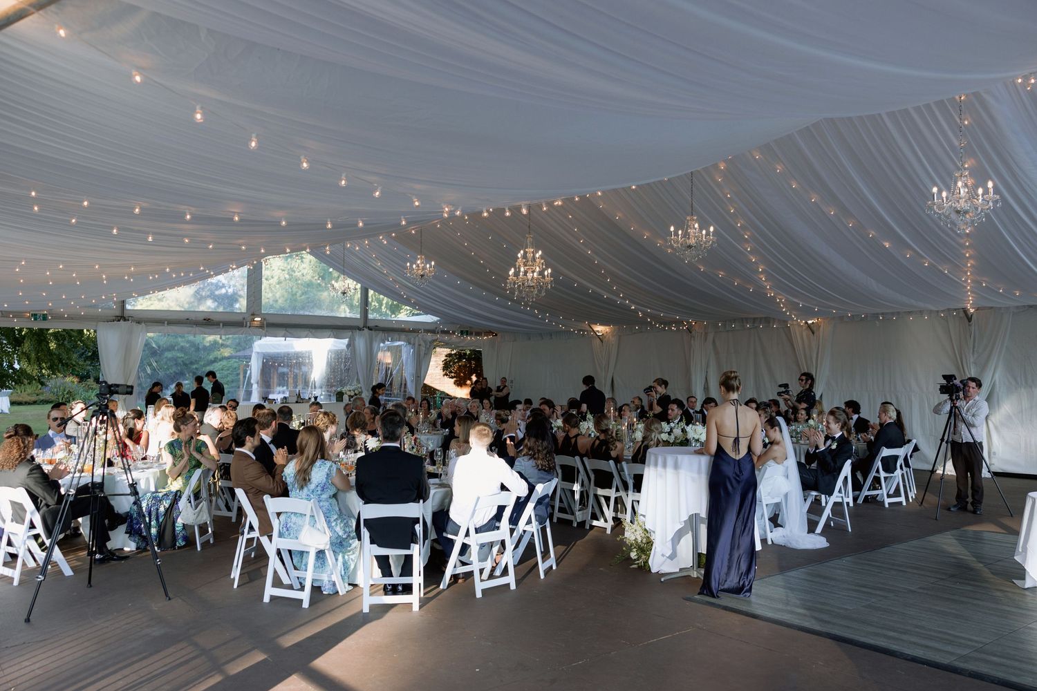 Elegant wedding reception venue with white tent ceiling, string lights, and round tables set for dining.