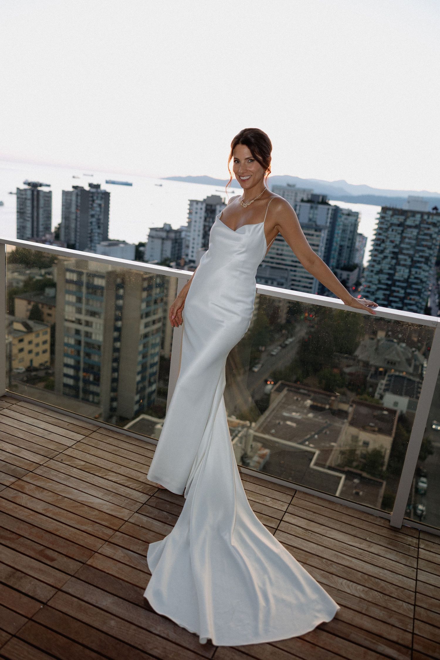 Elegant white wedding dress on balcony overlooking Vancouver cityscape.
