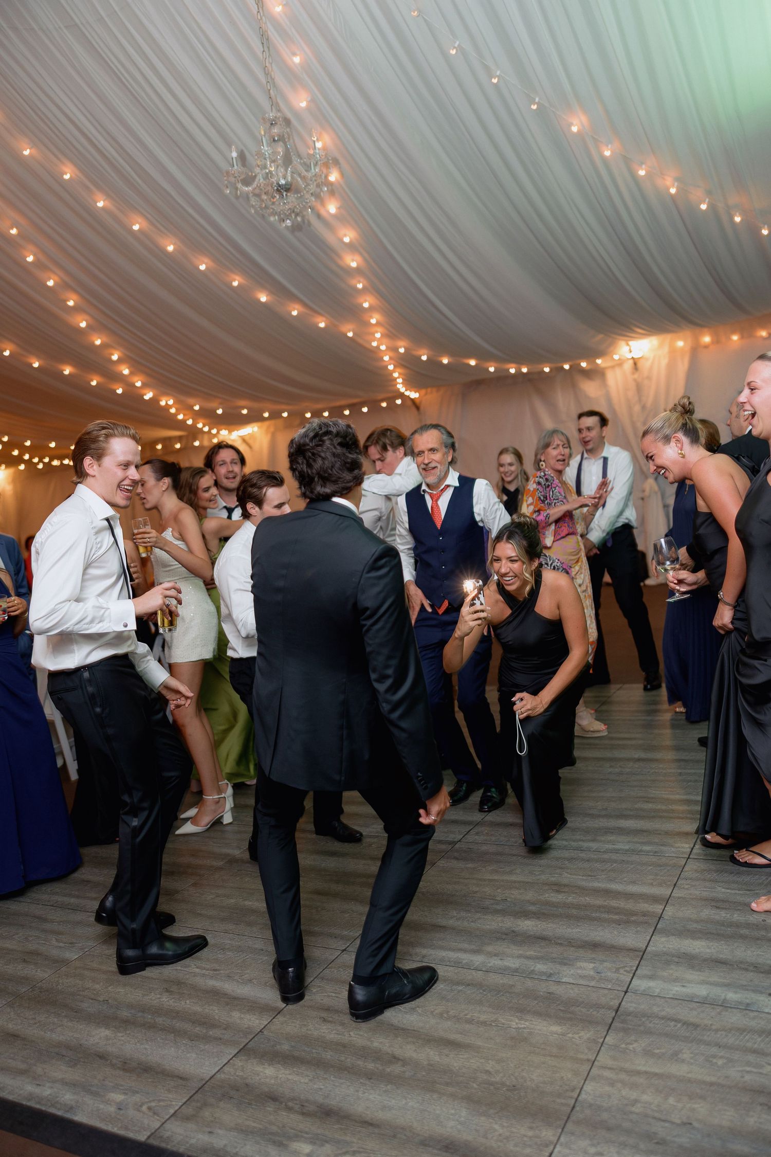 Energetic dancing at a formal wedding reception under twinkling tent lights.