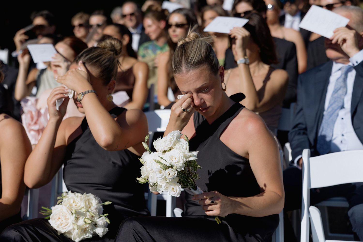 Guests seated at an outdoor wedding ceremony holding white programs.