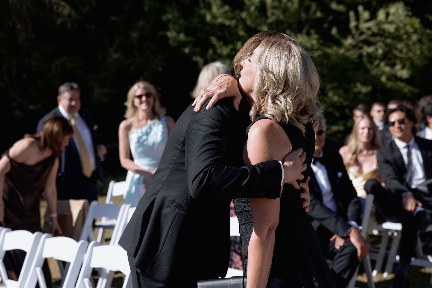 Wedding guests in formal attire stand together during an outdoor celebration.