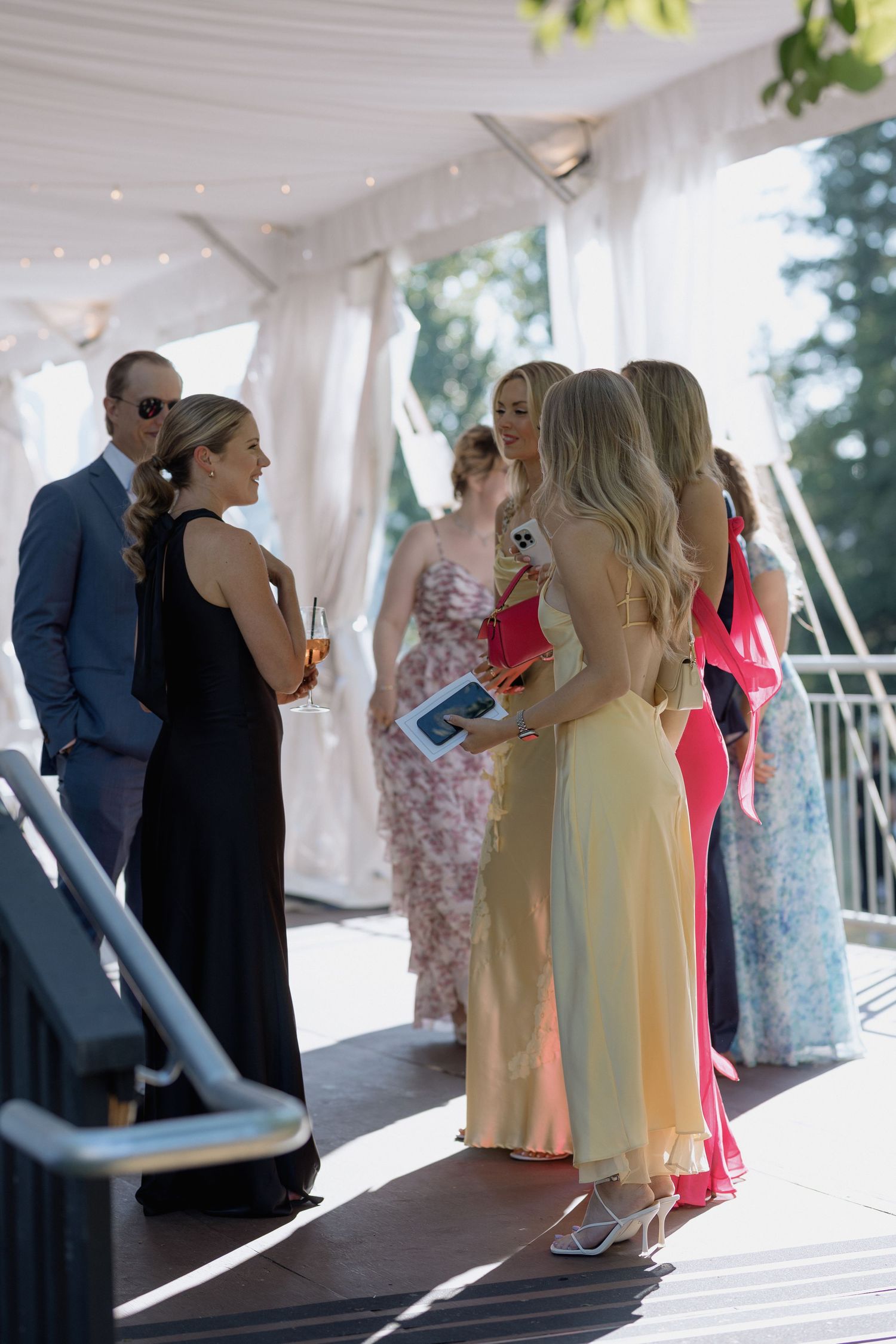Wedding guests mingle and socialize under a white tent during an outdoor reception.