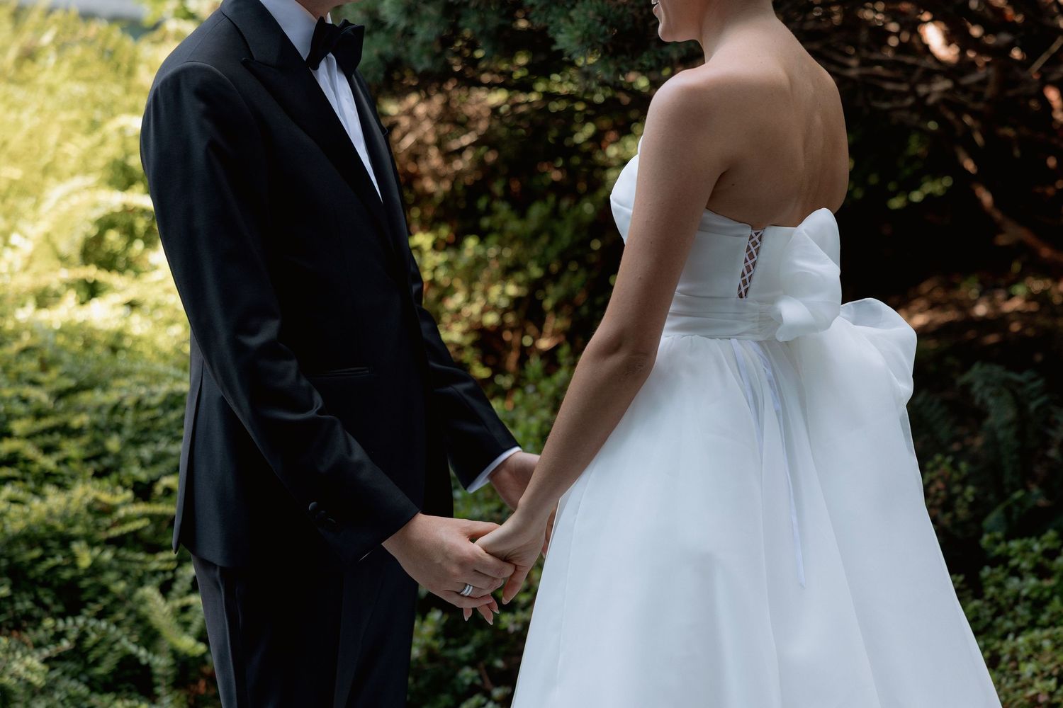 A tender moment between newlyweds holding hands in an intimate garden setting.