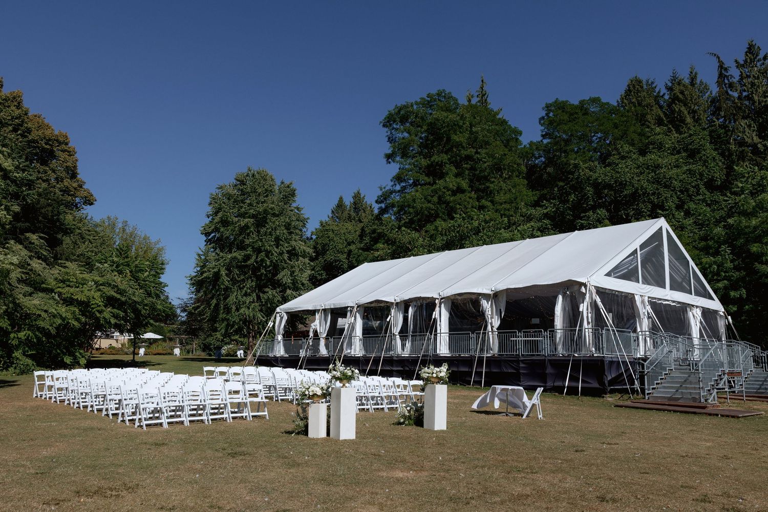 Large white wedding tent set up on a grassy hill with views of trees and water at Hurt House in Burnaby