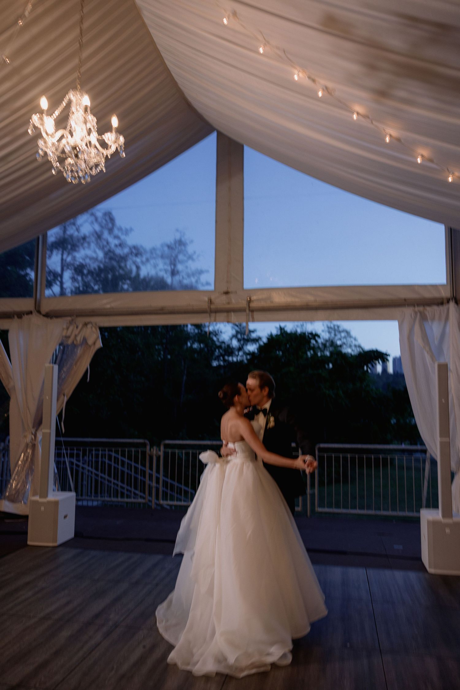 Wedding couple dancing in an elegant tent-covered venue at sunset.
