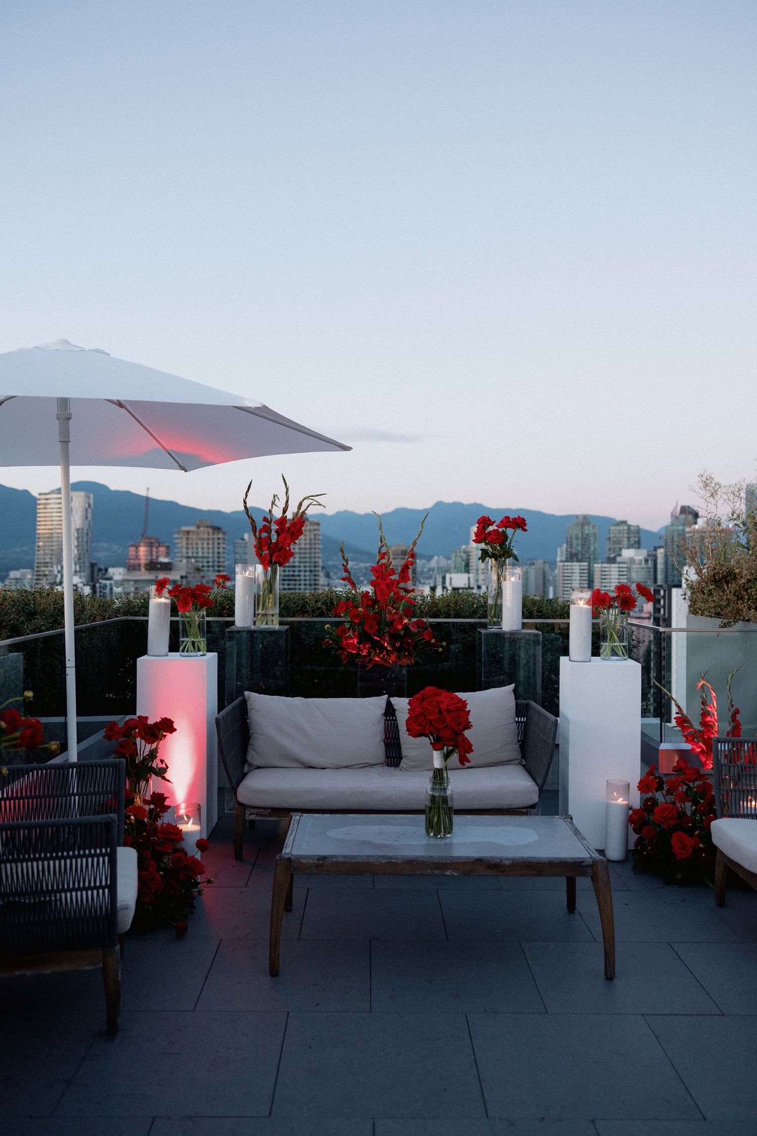 Rooftop lounge area with grey seating, red floral arrangements and city mountain views.