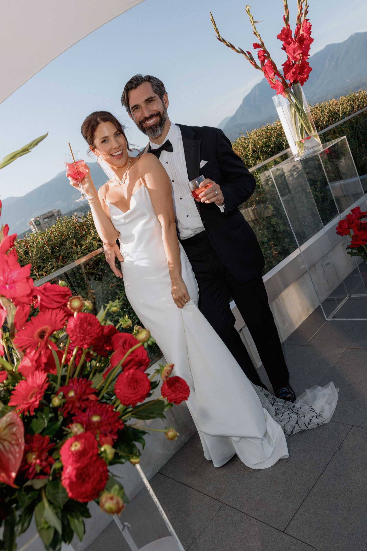Elegant rooftop wedding celebration with vibrant red flower arrangements and mountain views.