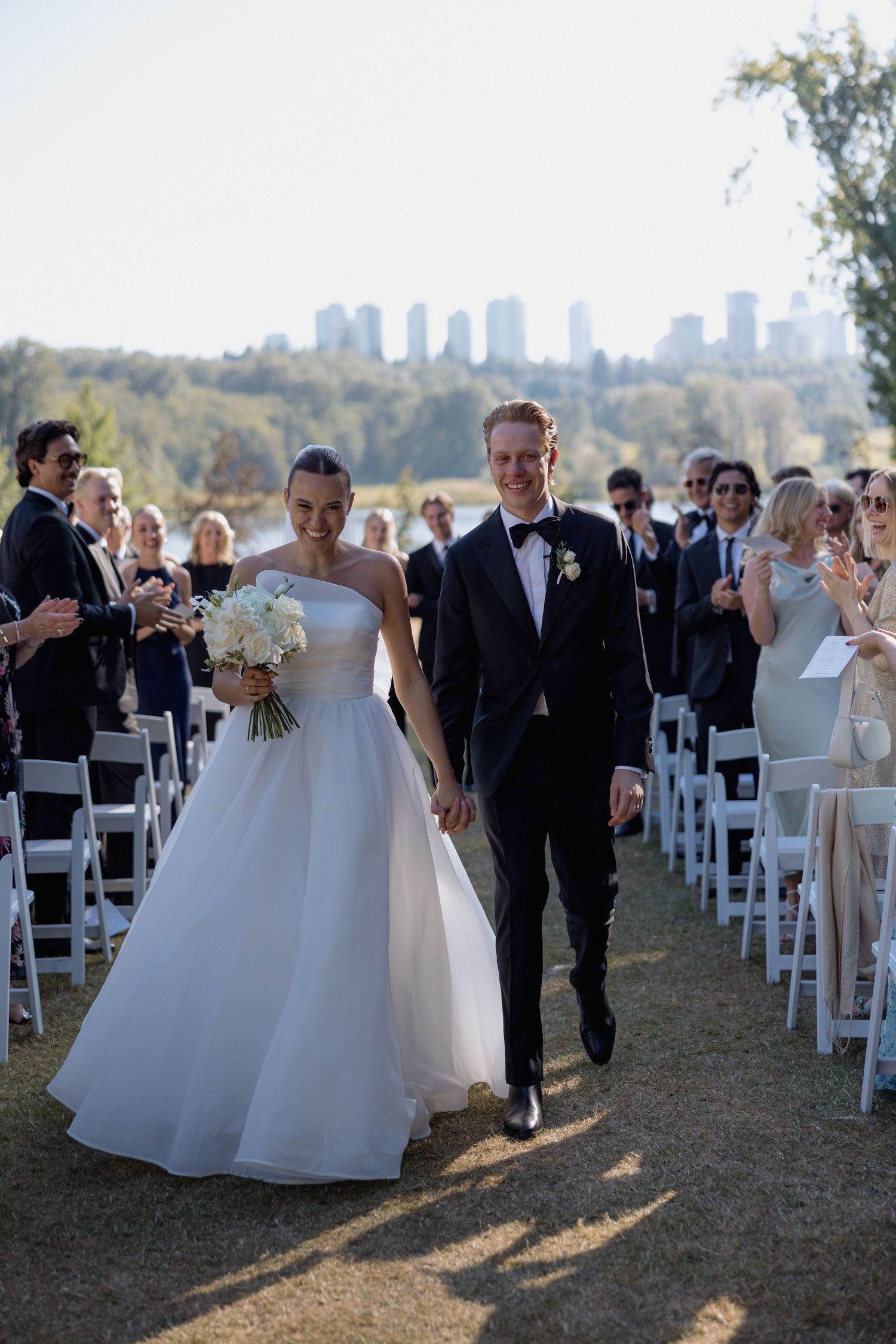 Wedding party walking down the aisle after ceremony with guests in white chairs and city views on the Deer Lake