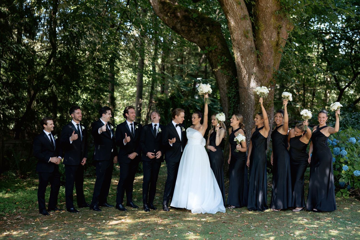 Wedding party arranged in a diagonal line under shady trees for outdoor photos.