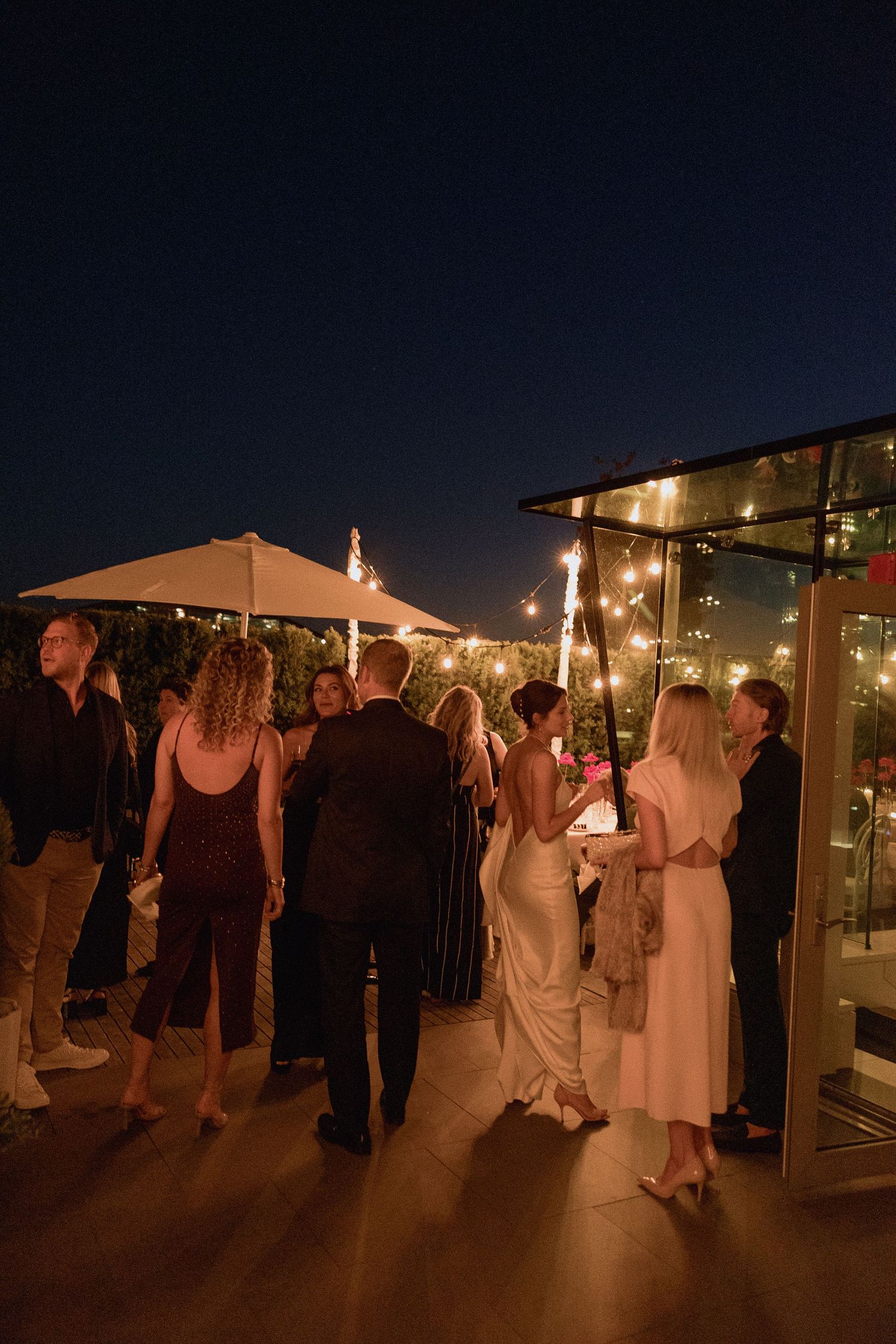 Wedding guests mingling on a rooftop terrace under string lights at night in the night of Vancouver
