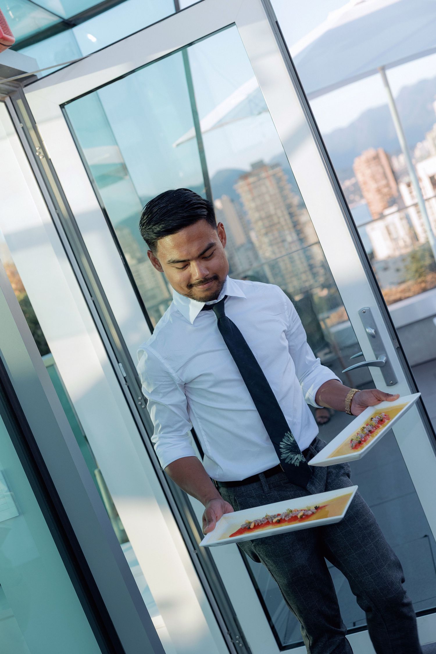 Server in formal attire carrying plates of food at an outdoor event.