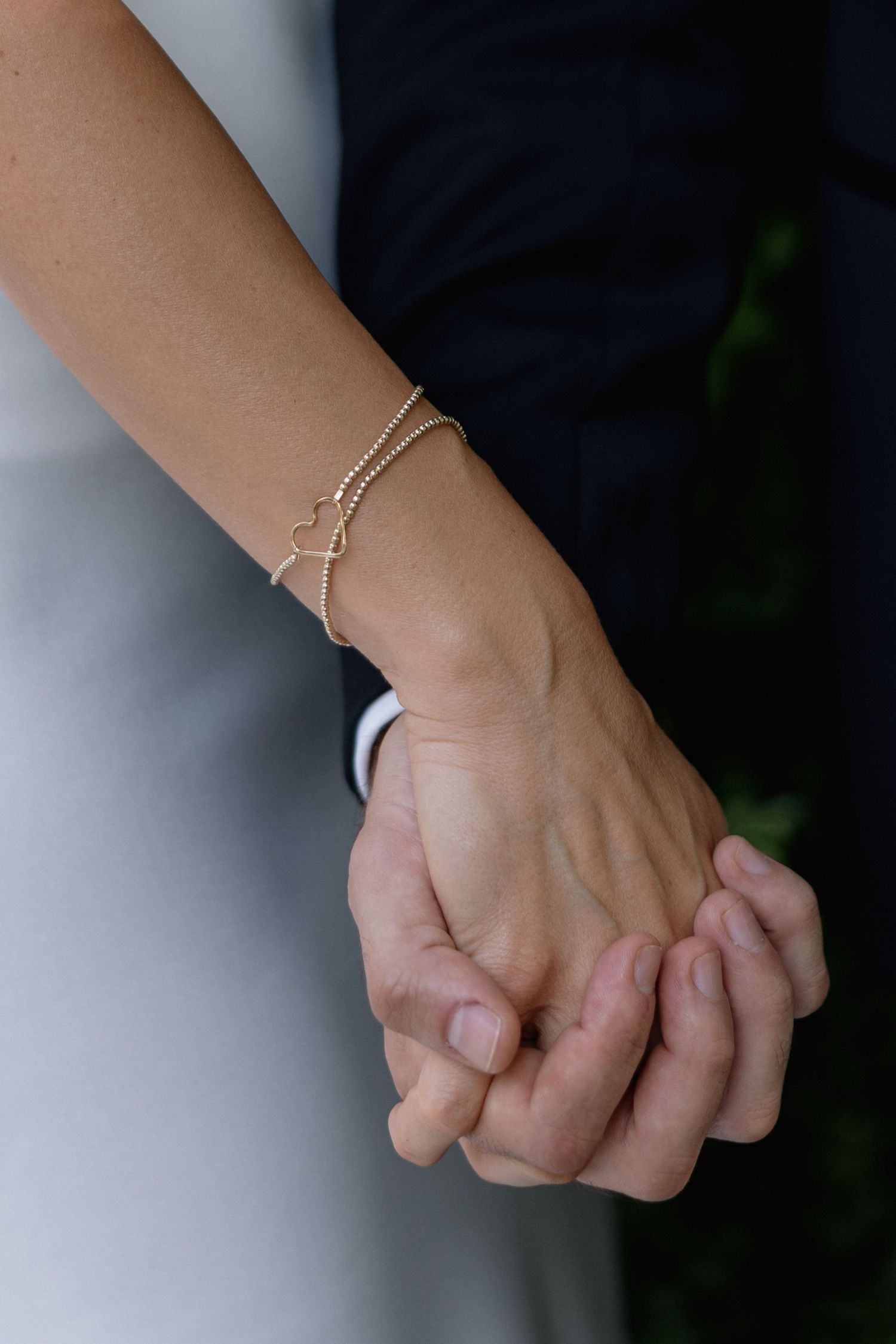 Close-up of two hands holding each other with a delicate gold bracelet visible on one wrist.