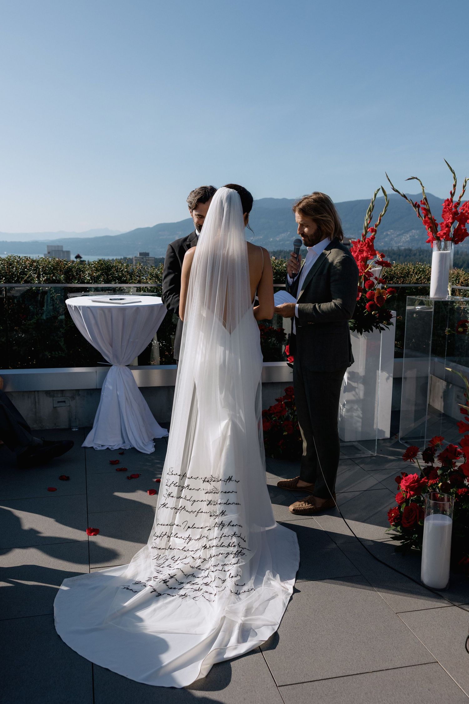 Outdoor rooftop wedding ceremony with mountain views and red floral arrangements.