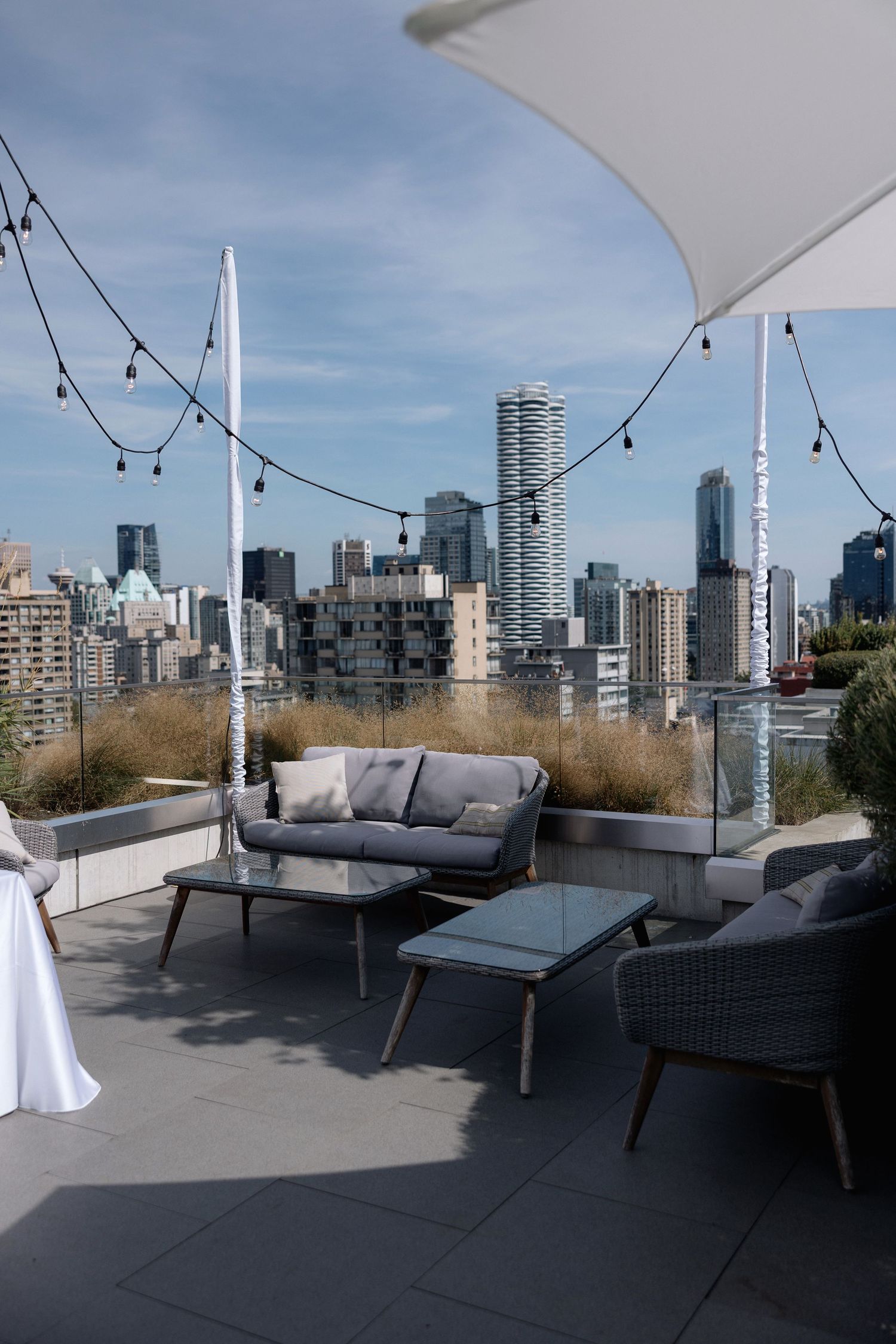 Modern rooftop patio with grey outdoor furniture and string lights overlooking Vancouver's downtown skyline.