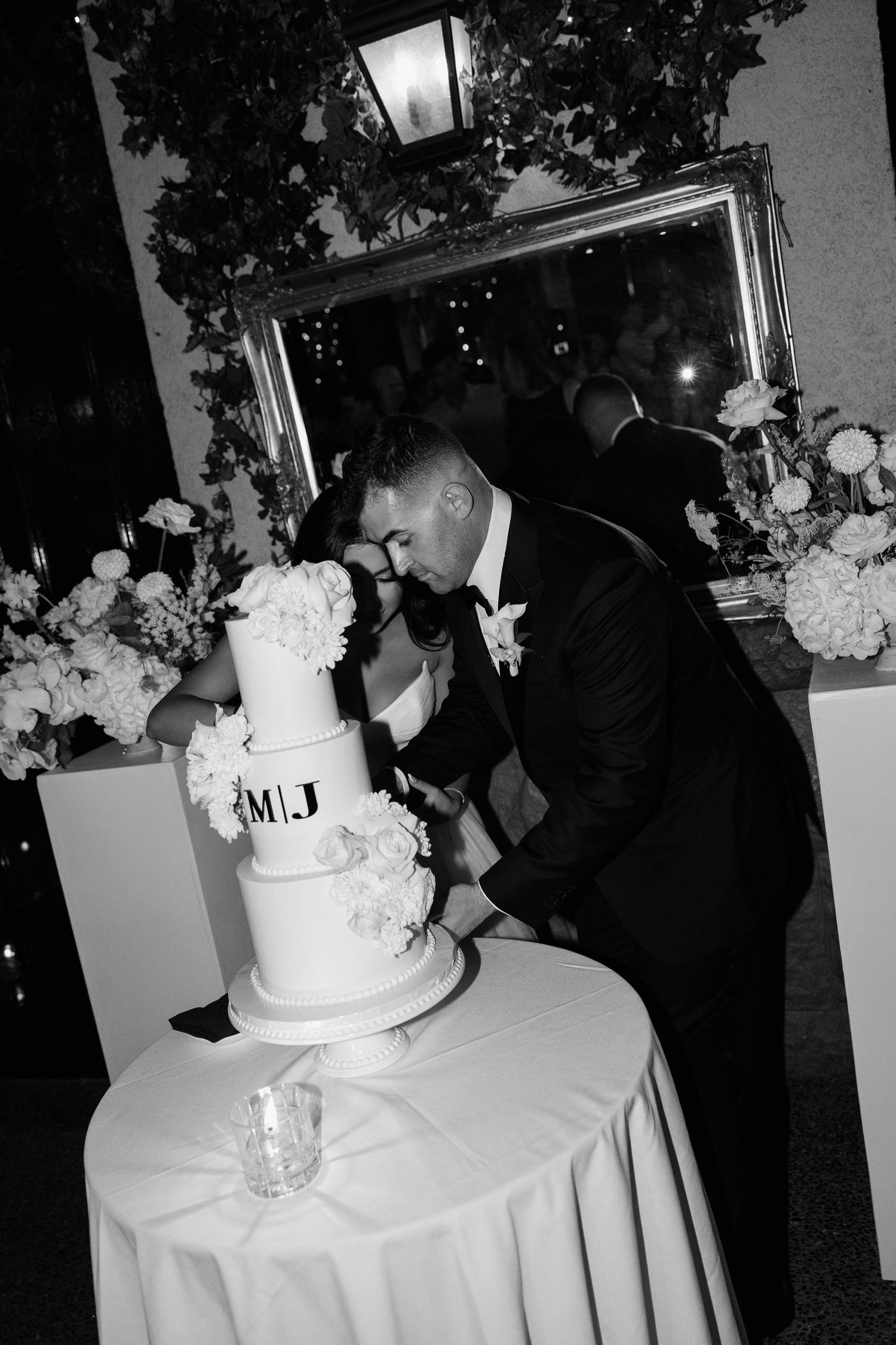 A sequence of black and white wedding photos showing a couple cutting their traditional white tiered wedding cake.