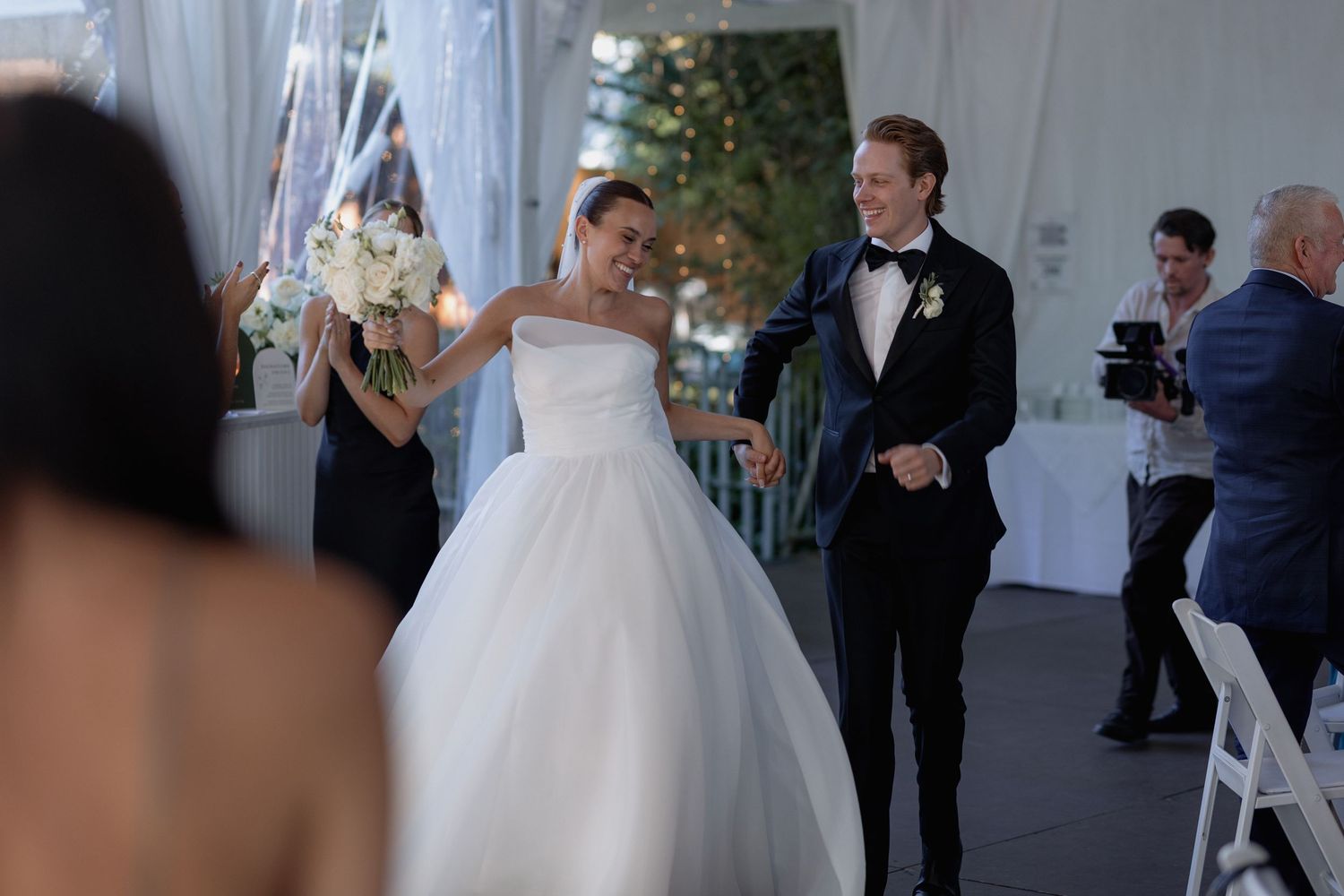 Wedding guests mingling inside elegant white tent reception space.
