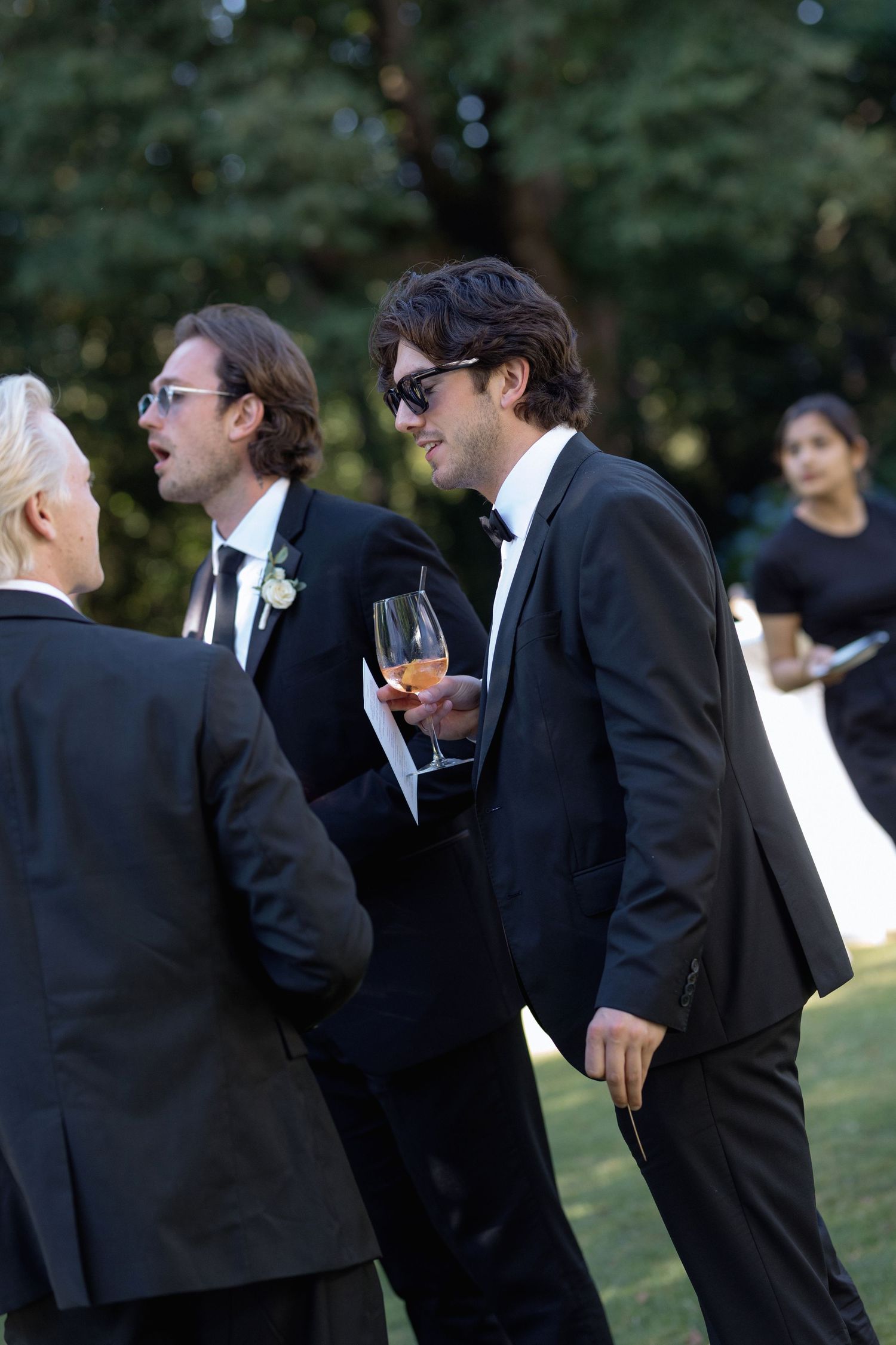 Guests in formal attire enjoying drinks and conversation at an outdoor wedding reception.
