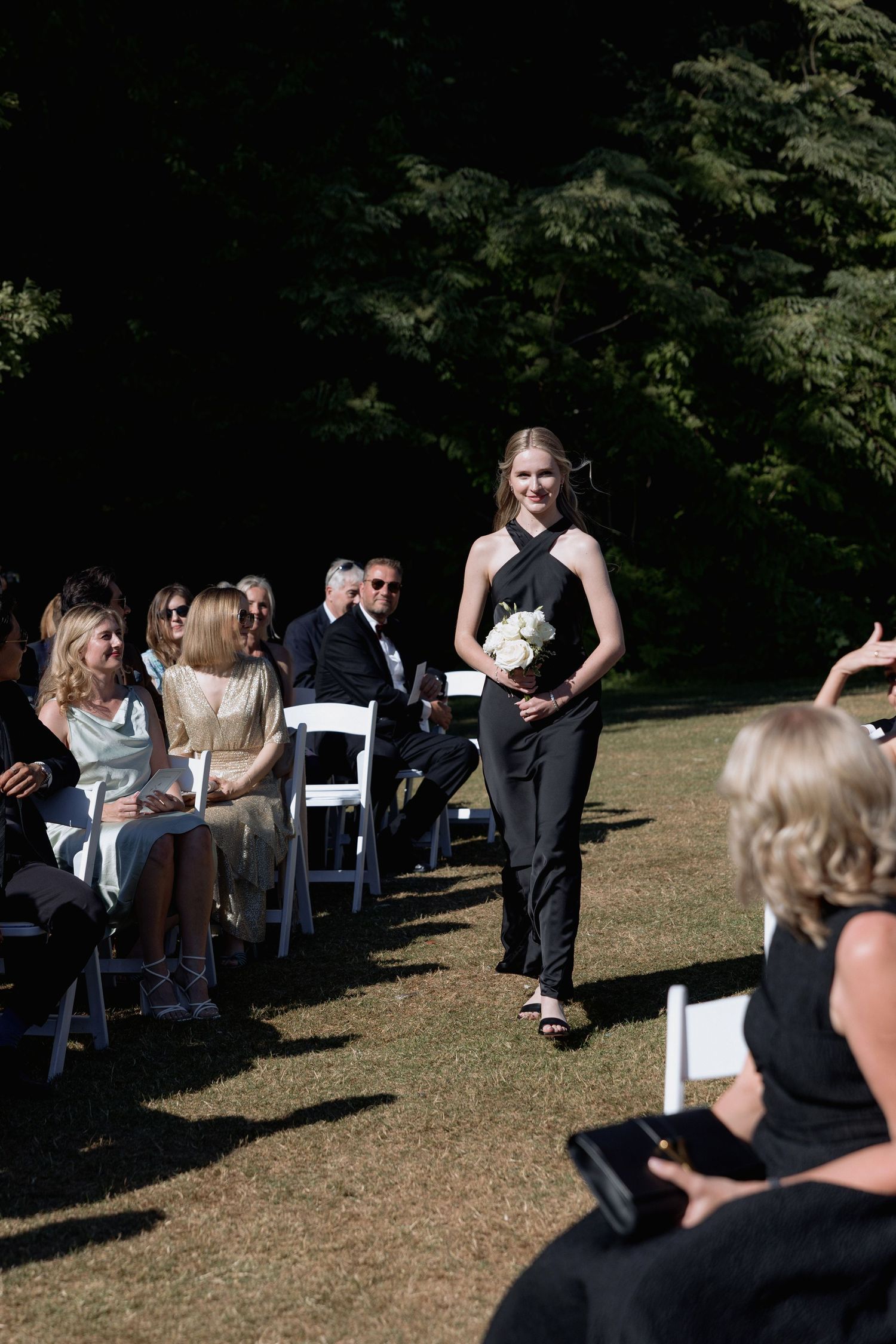 Guests seated in white chairs on a lawn during an outdoor wedding ceremony.