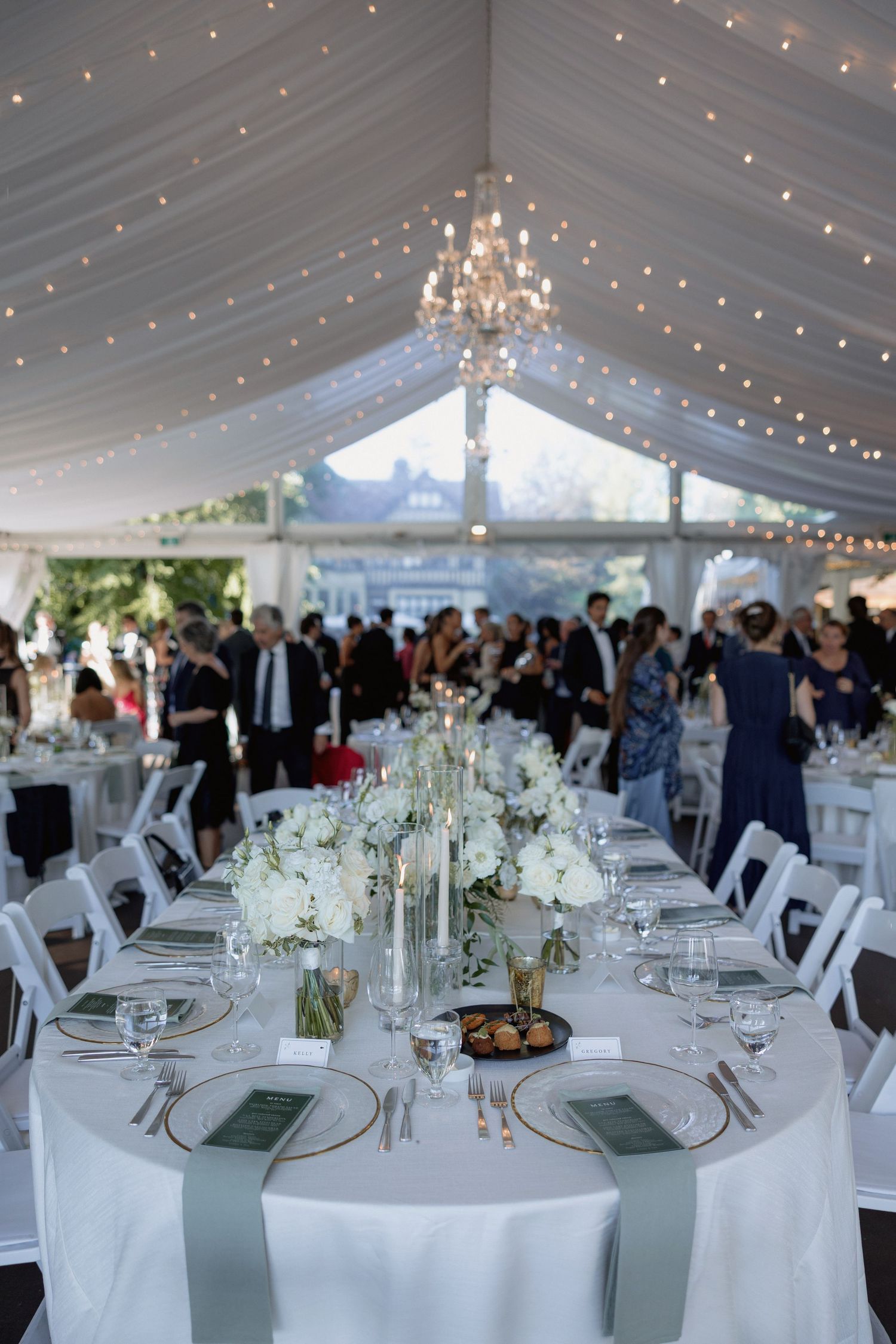 Elegant wedding reception table setting with crystal chandelier and string lights in white tent Hurt House in Burnaby