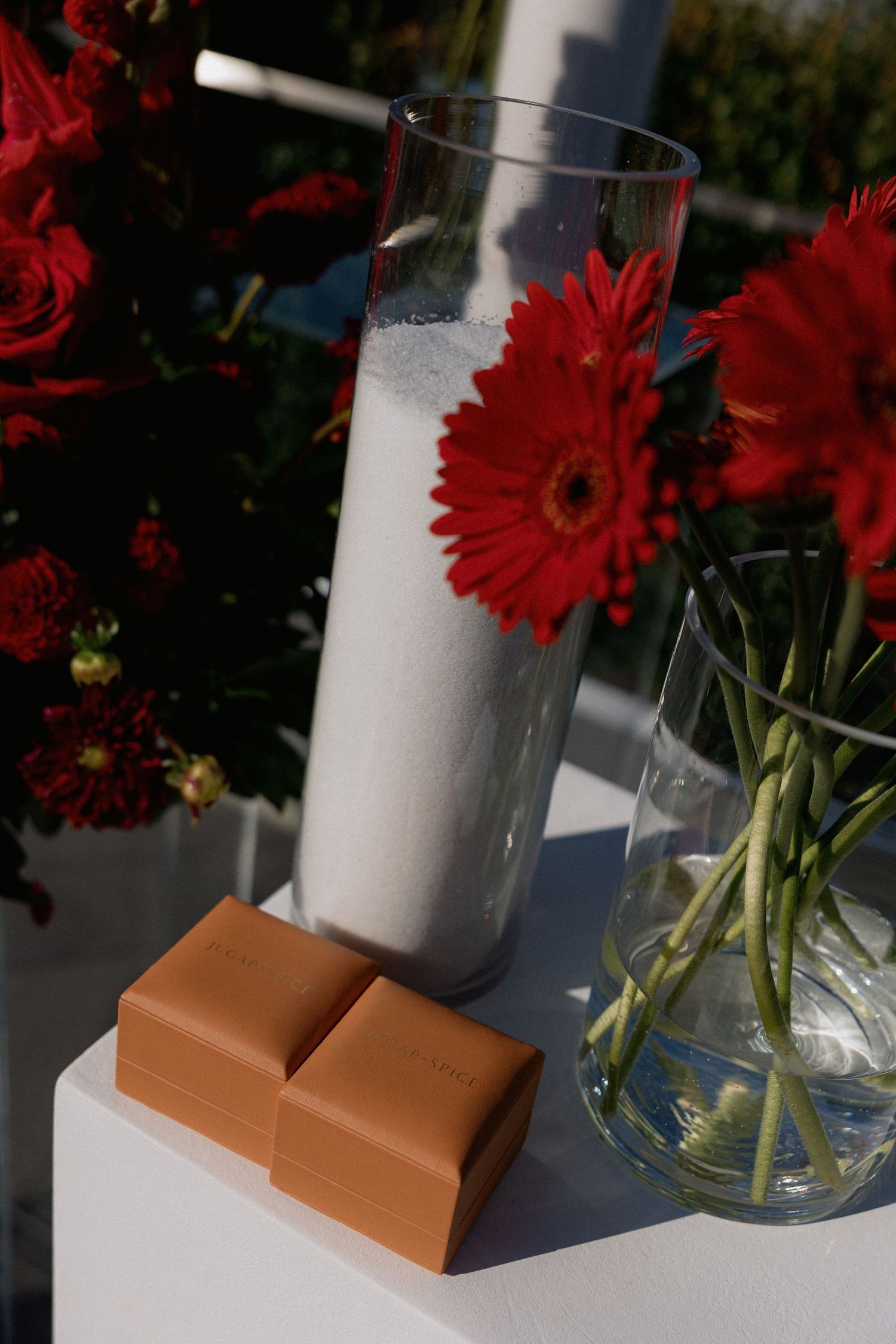 Red gerbera daisy and roses displayed with milk glass and caramel chocolates on white surface.