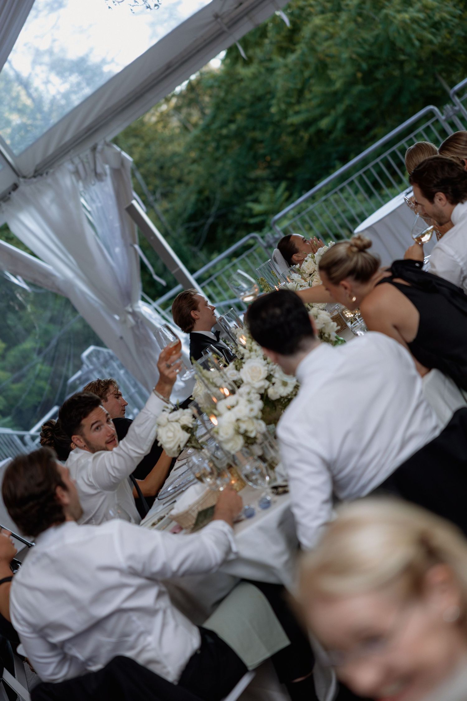 Wedding reception guests seated at tables under a white tent enjoying dinner and conversation.