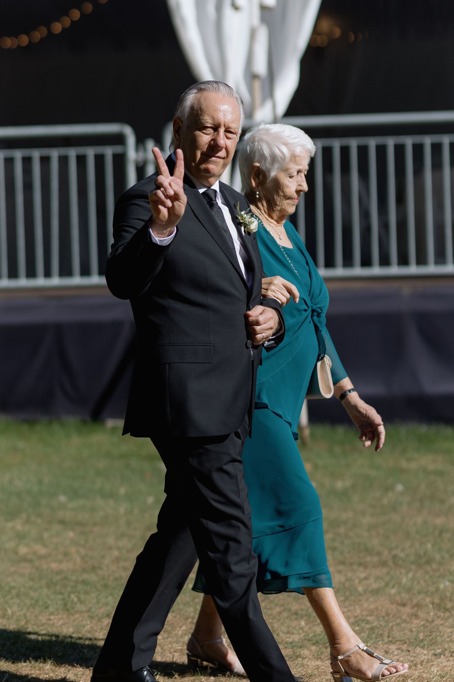 Formal wedding attendees walking together on grass near white tent.