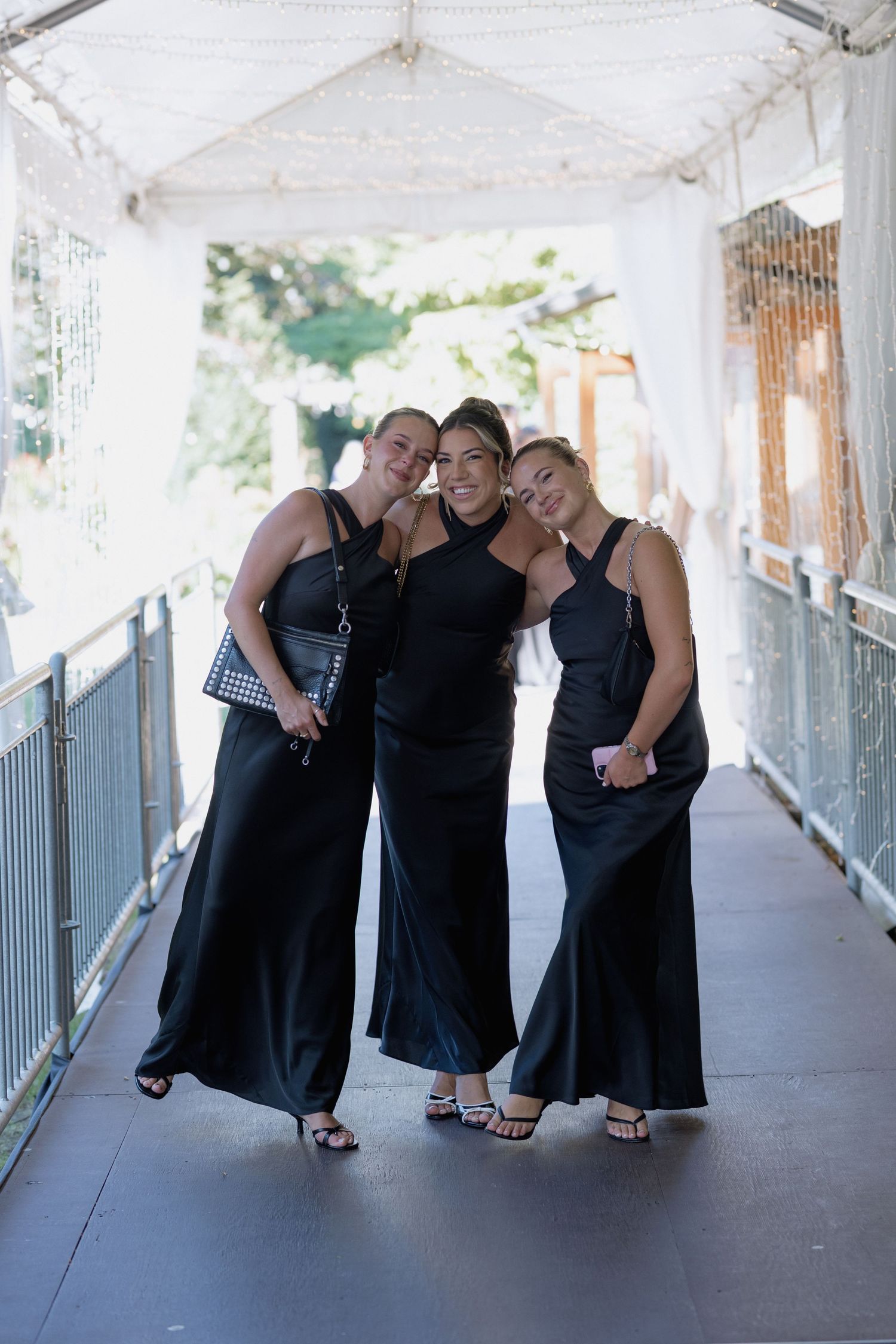 Bridesmaids in matching black dresses pose playfully in a covered walkway at a wedding venue.