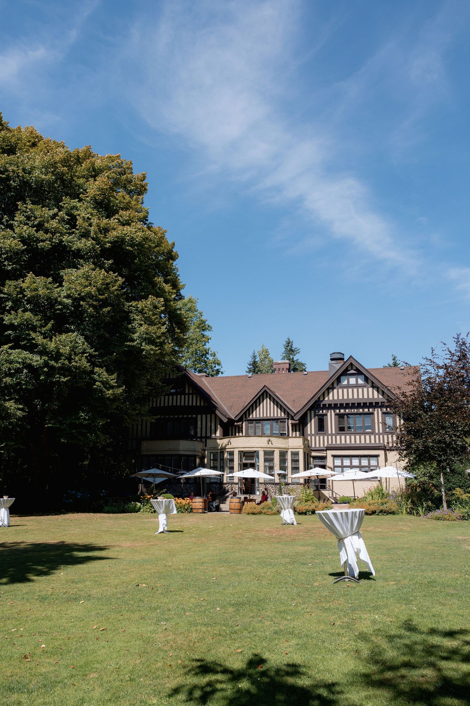 Tudor-style mansion with white decorations on lawn under blue summer sky at Hurt House in Burnaby