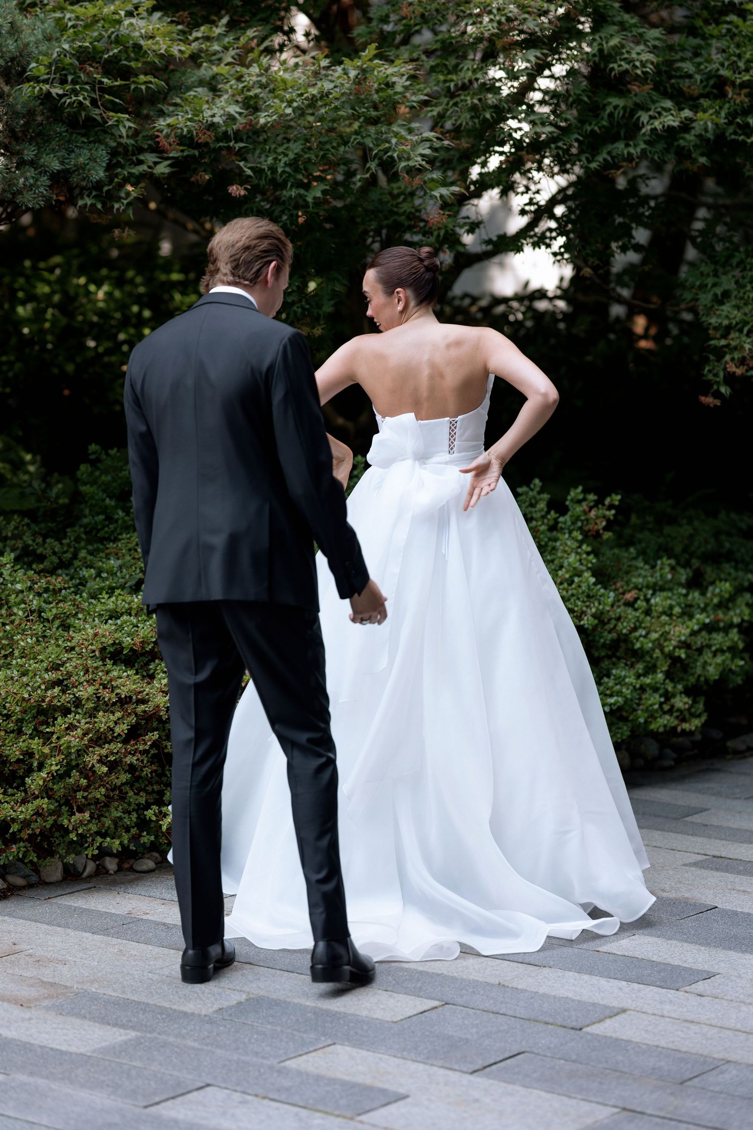 A wedding couple standing together on grey stone pavers surrounded by garden landscaping.