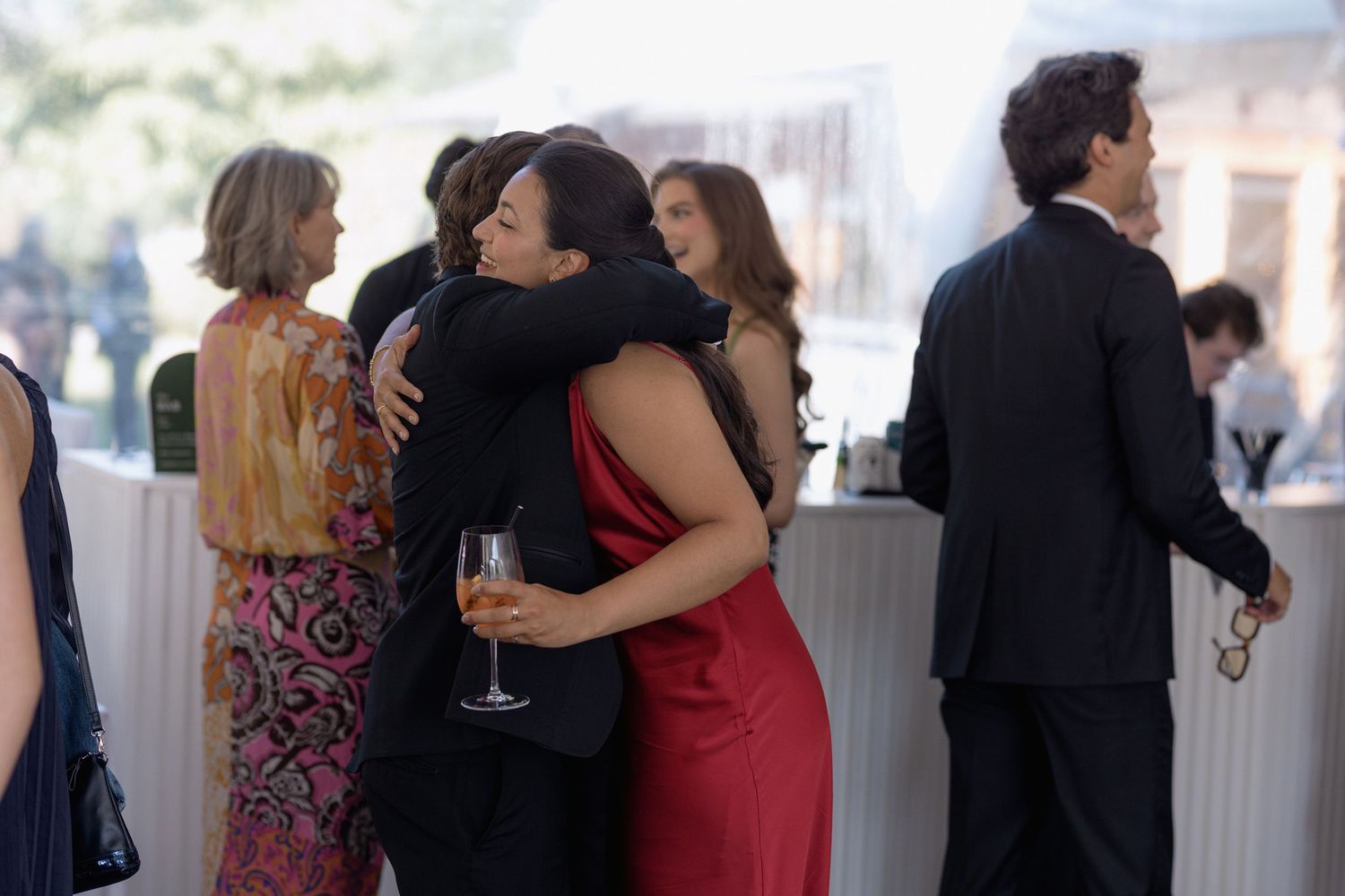 Guests sharing warm embraces during a formal event under a tent.