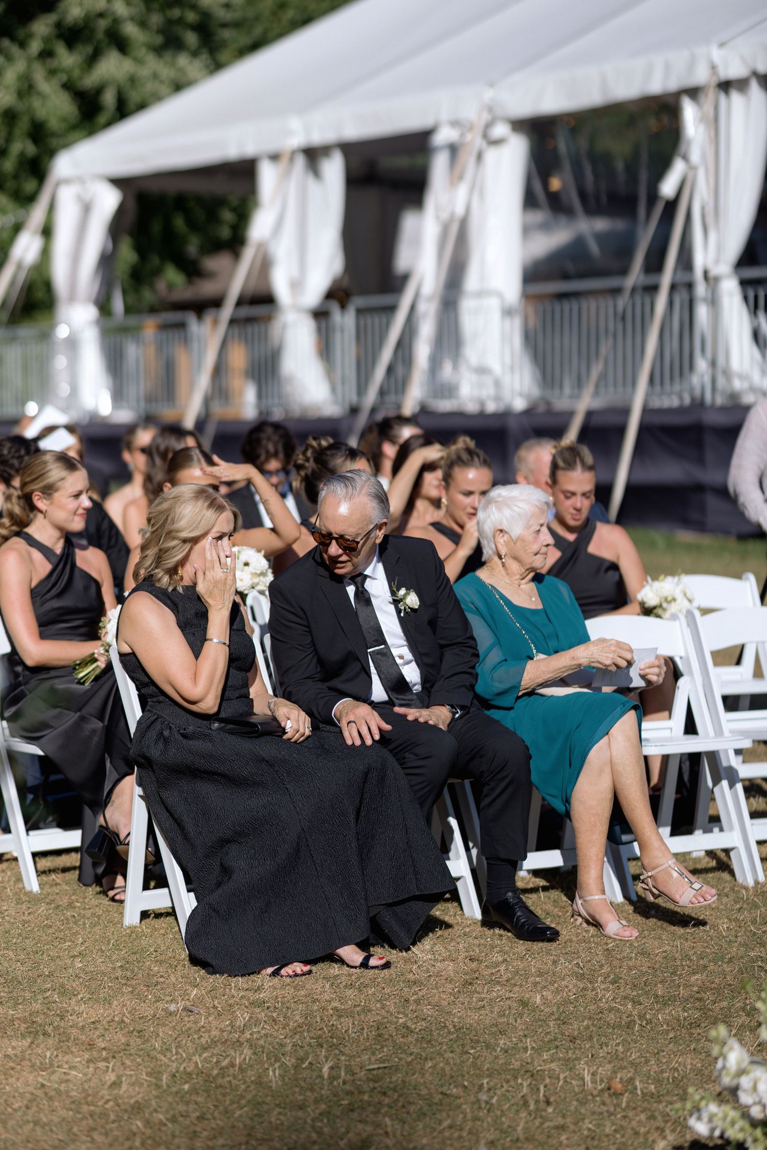 Wedding guests seated in white chairs under white tents during an outdoor celebration.