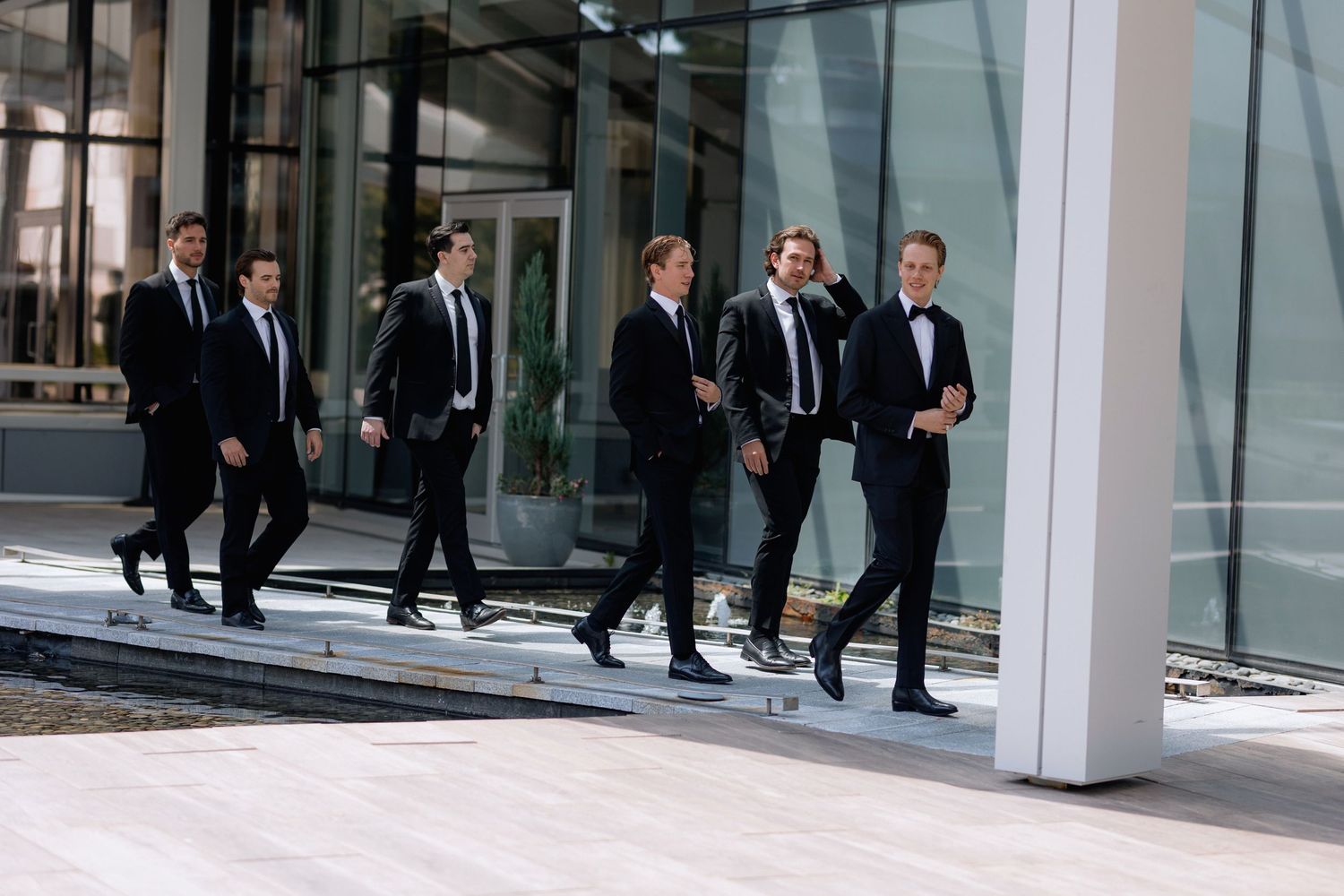 Group walking in formal suits through modern glass-walled building corridor at Marriott Hotel in Vancouver