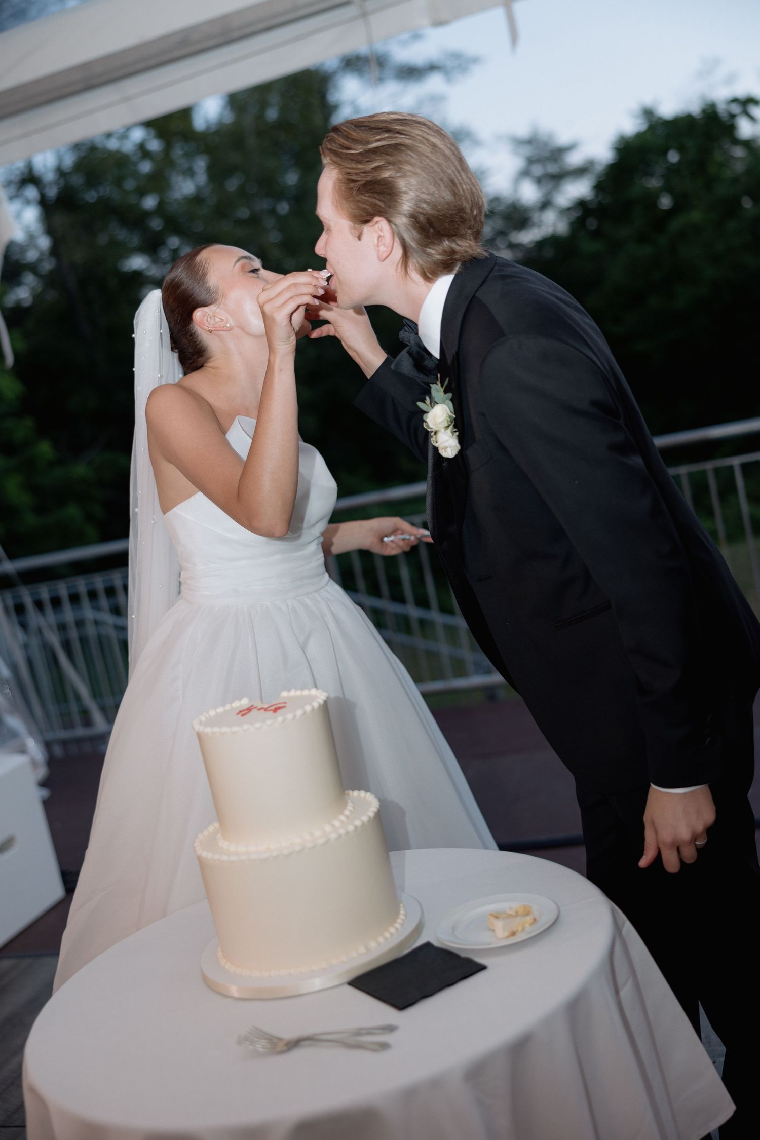 A couple sharing their first bite of wedding cake during an outdoor reception.