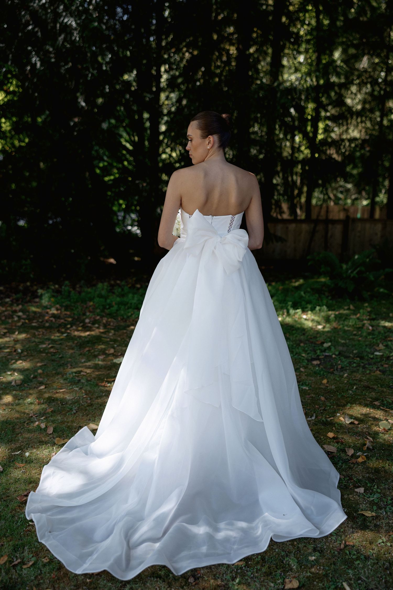 Back view of flowing white wedding dress with train spread out on autumn leaves.