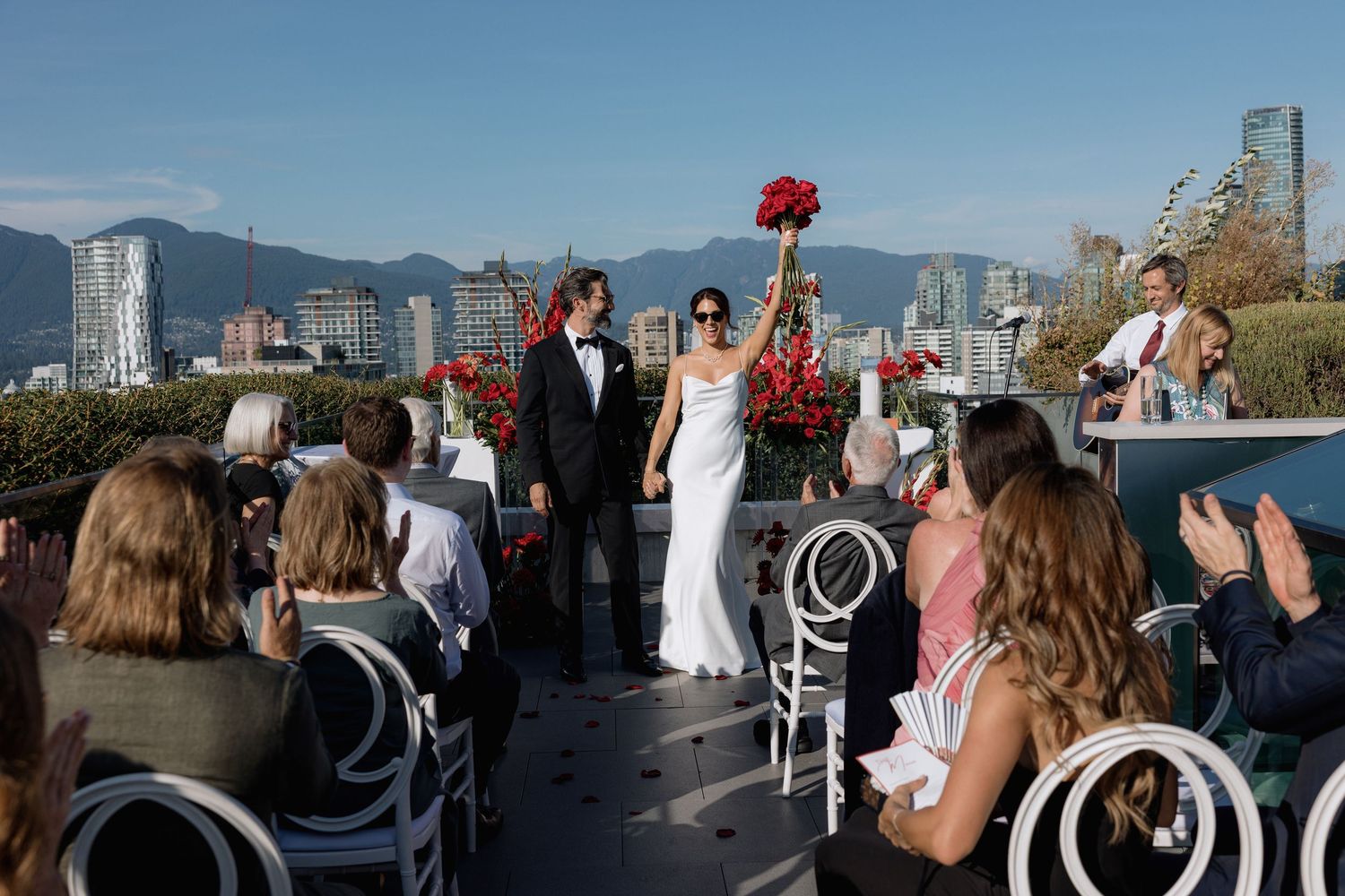 Wedding guests mingling on a rooftop terrace with mountain views and red floral decorations.