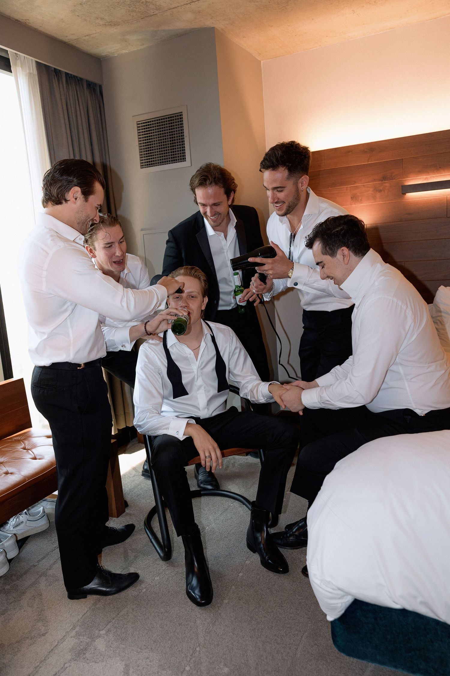 Group in formal white shirts and black pants sharing a lighthearted moment in a hotel room.