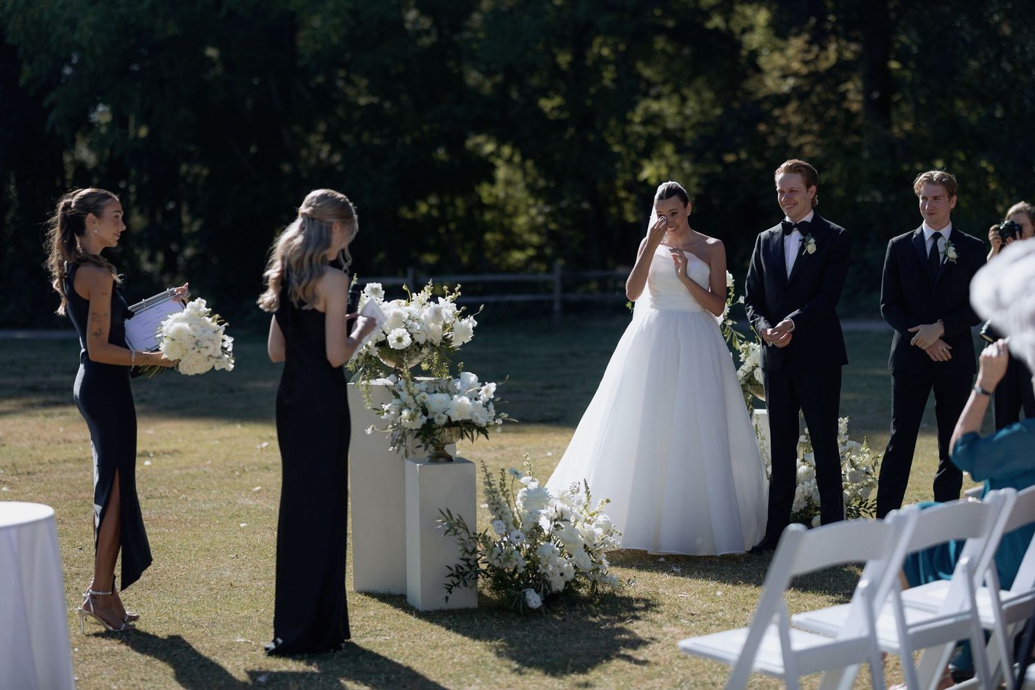 Outdoor wedding ceremony with floral arrangements and guests in formal attire.