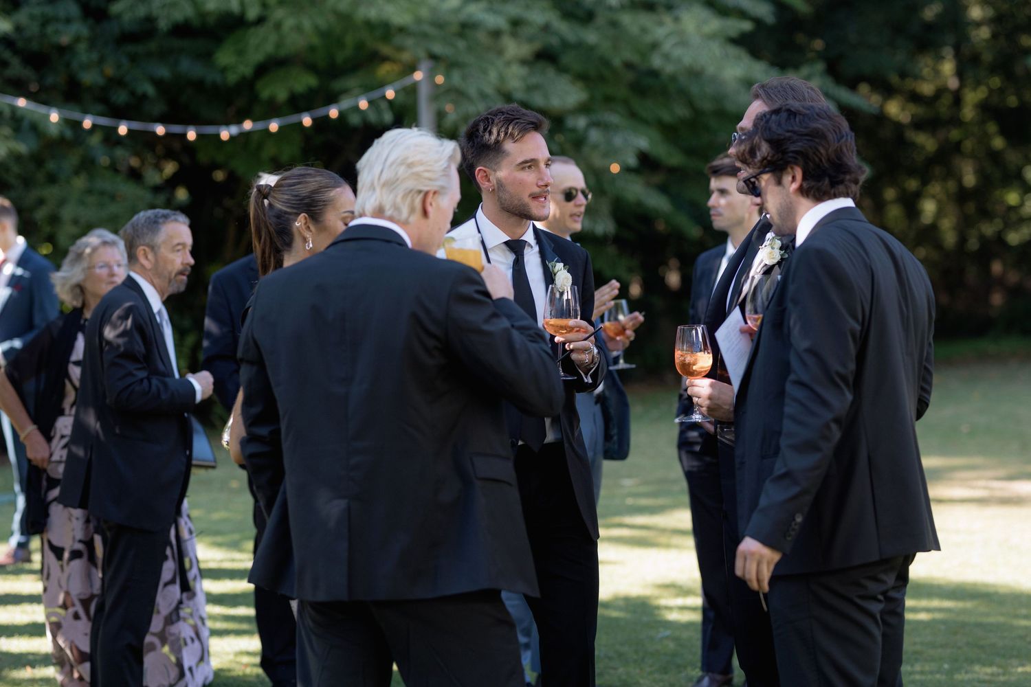 Evening wedding reception with string lights and guests mingling outdoors.
