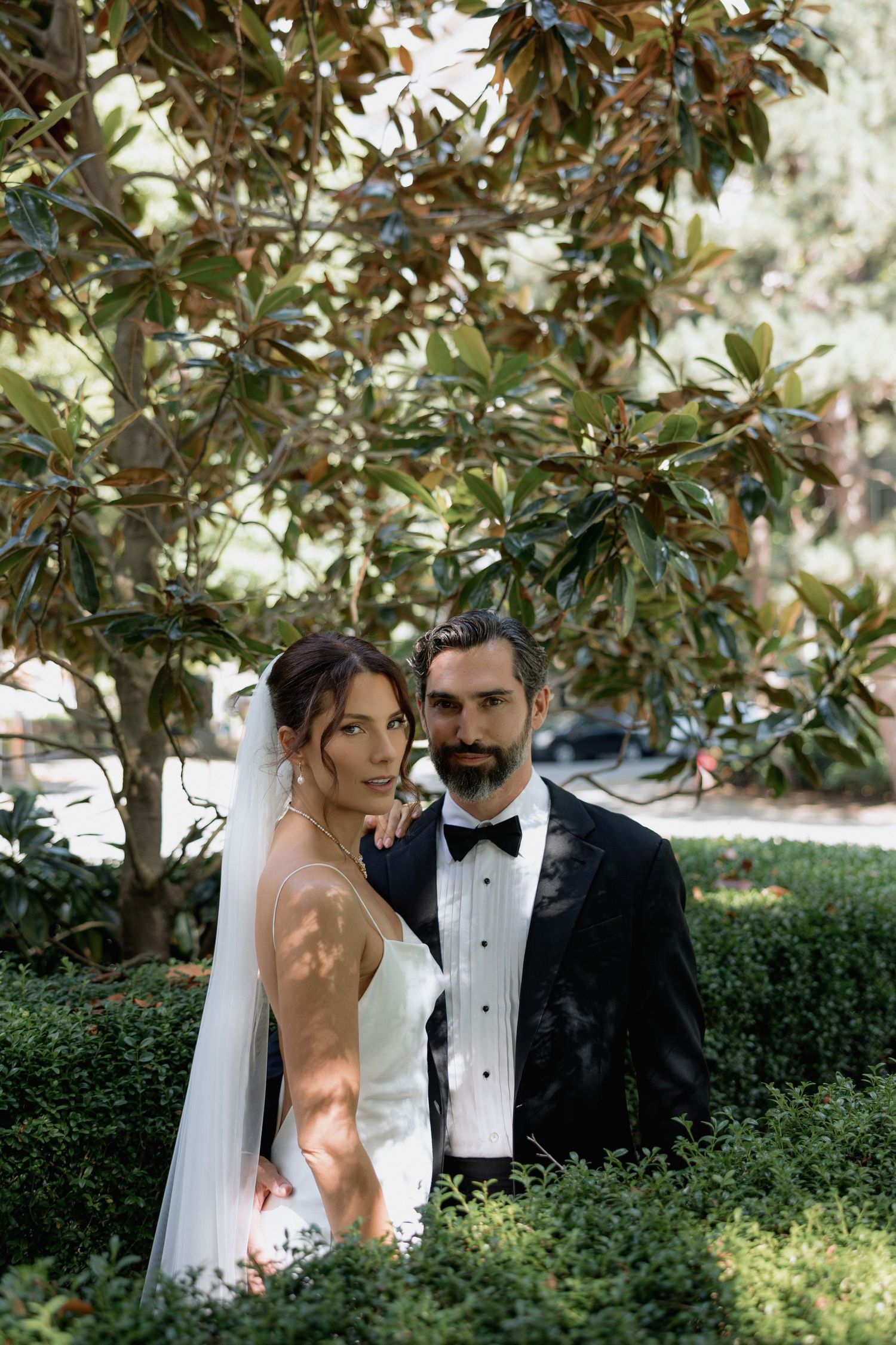 A couple poses under a magnolia tree in formal wedding attire on their special day.