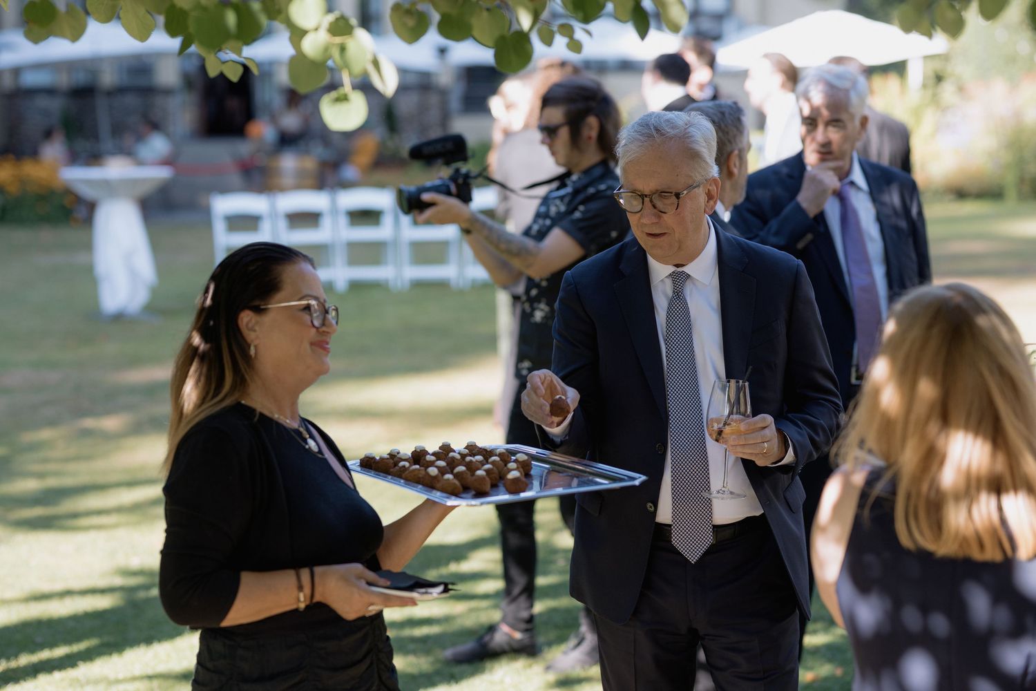 Wedding guests chat and mingle on a sunny lawn during an outdoor reception.