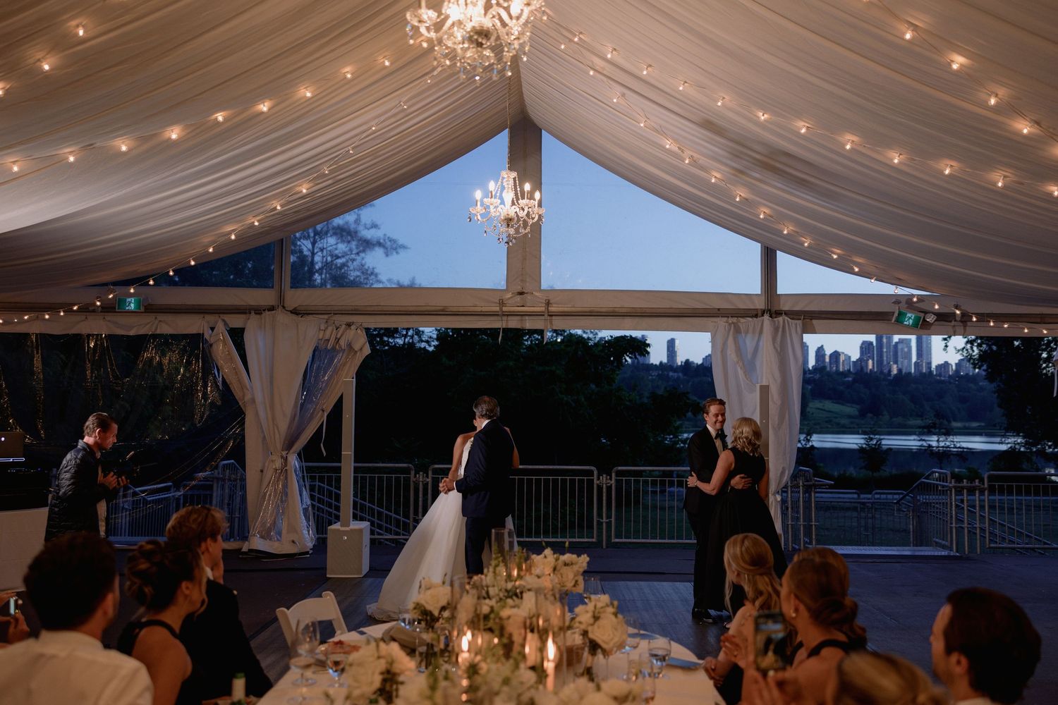 Elegant wedding reception under a draped tent with chandeliers and string lights creating a romantic atmosphere.