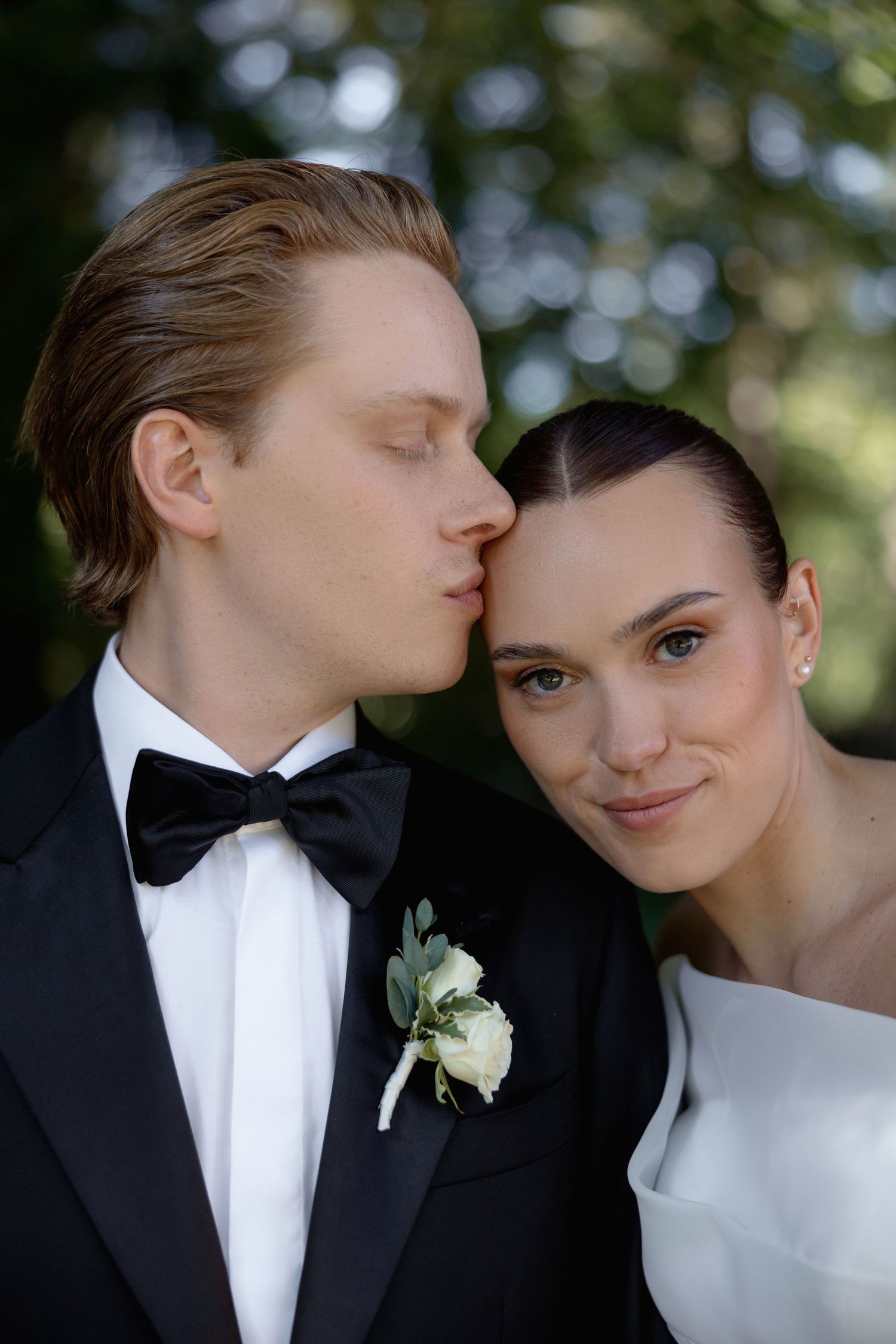 Romantic wedding portrait with soft bokeh background and white rose boutonniere detail.